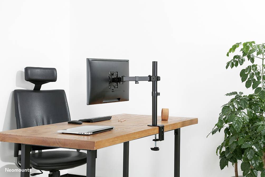 Ein moderner Schreibtisch mit einem Bürostuhl, einem Laptop, Bildschirm auf einem Arm, und einer Pflanze rechts.