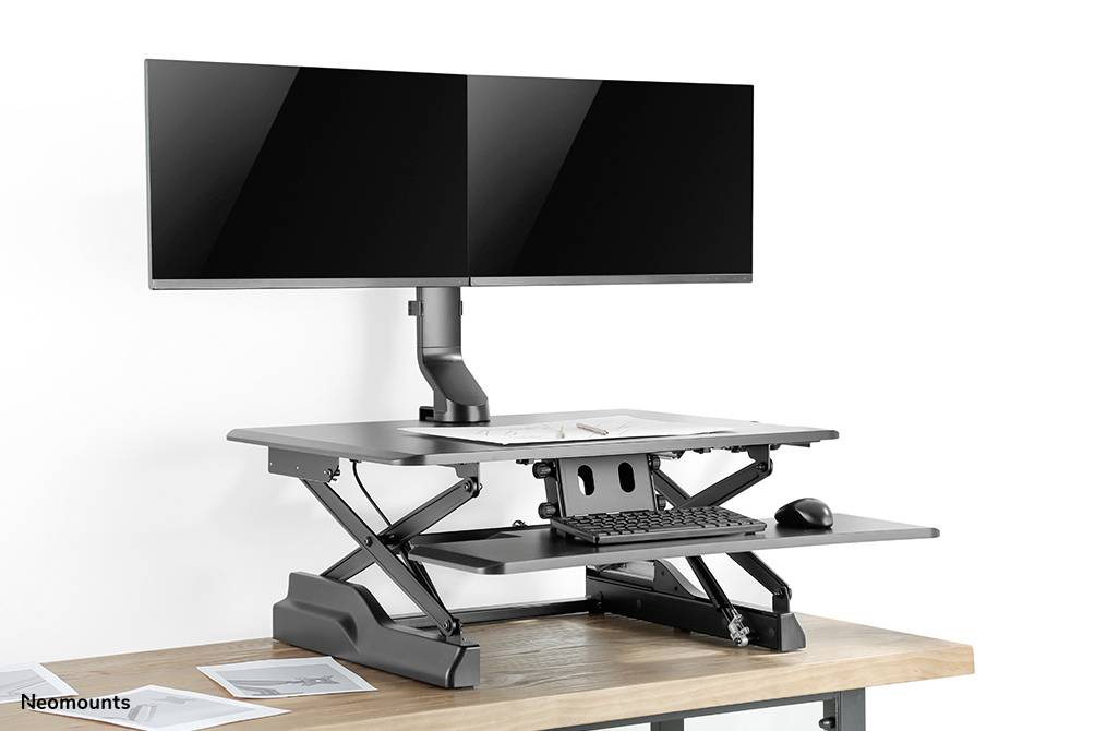 Höhenverstellbarer Schreibtischaufsatz aus Metall auf Holzschreibtisch mit zwei Monitoren, Tastatur und Maus.