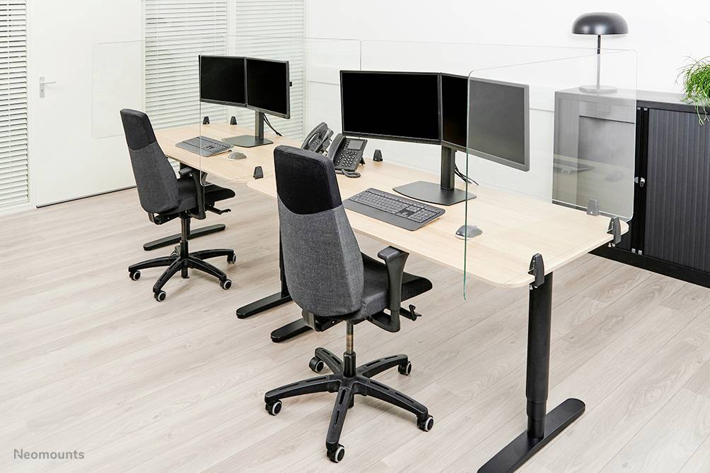 Zwei moderne Bürotische mit Computern, Monitoren und ergonomischen Stühlen; durch Glasabtrennungen getrennt, in einem Büro.