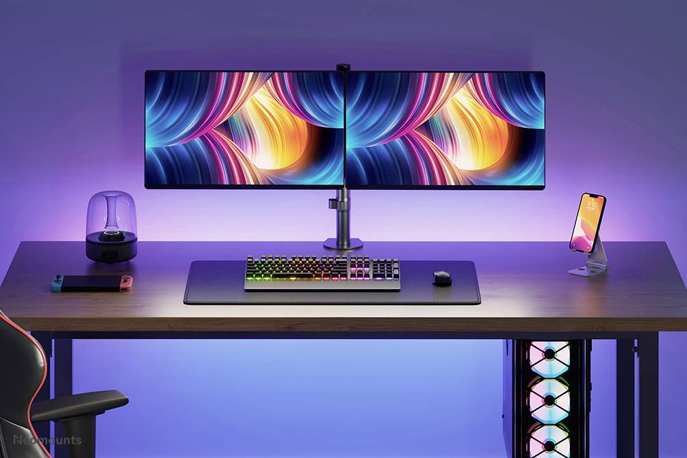 Ein Schreibtisch mit zwei großen Monitoren, einer farbenfrohen Tastatur, einer Maus und einem Smartphone auf einem Ständer. Im Hintergrund bunte LED-Beleuchtung.