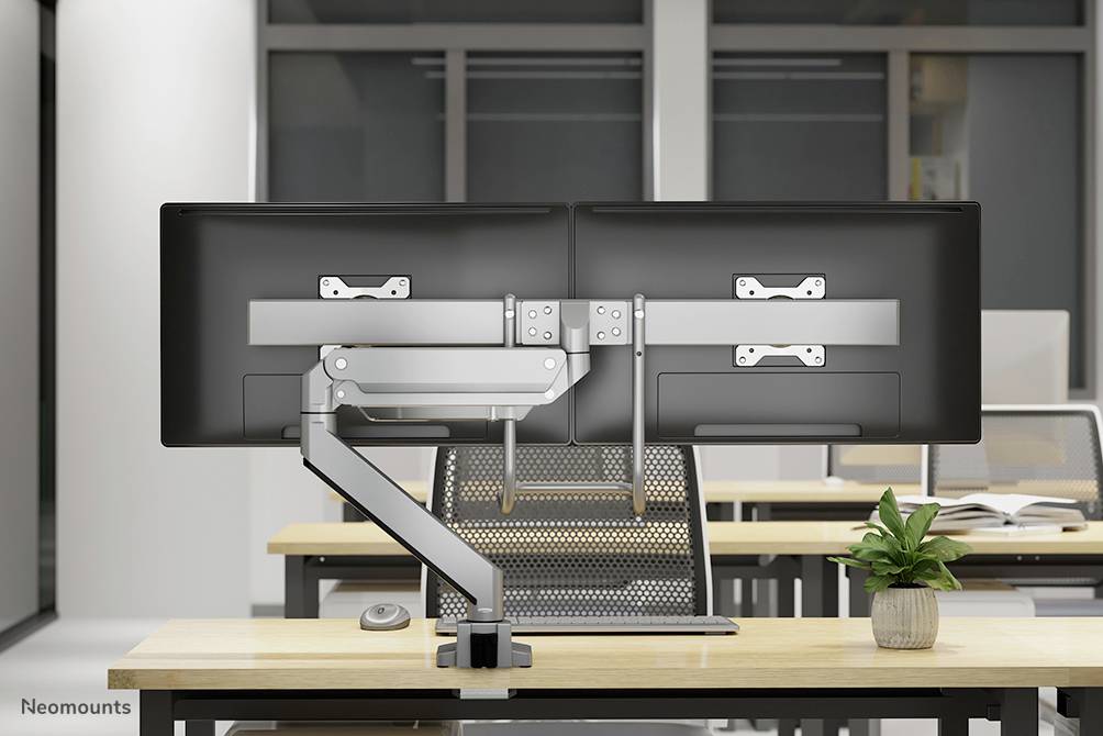 Zwei Monitore auf einem Schreibtisch sind an einer Dual-Monitorhalterung montiert. Ein kleiner grüner Pflanzenkübel steht daneben.