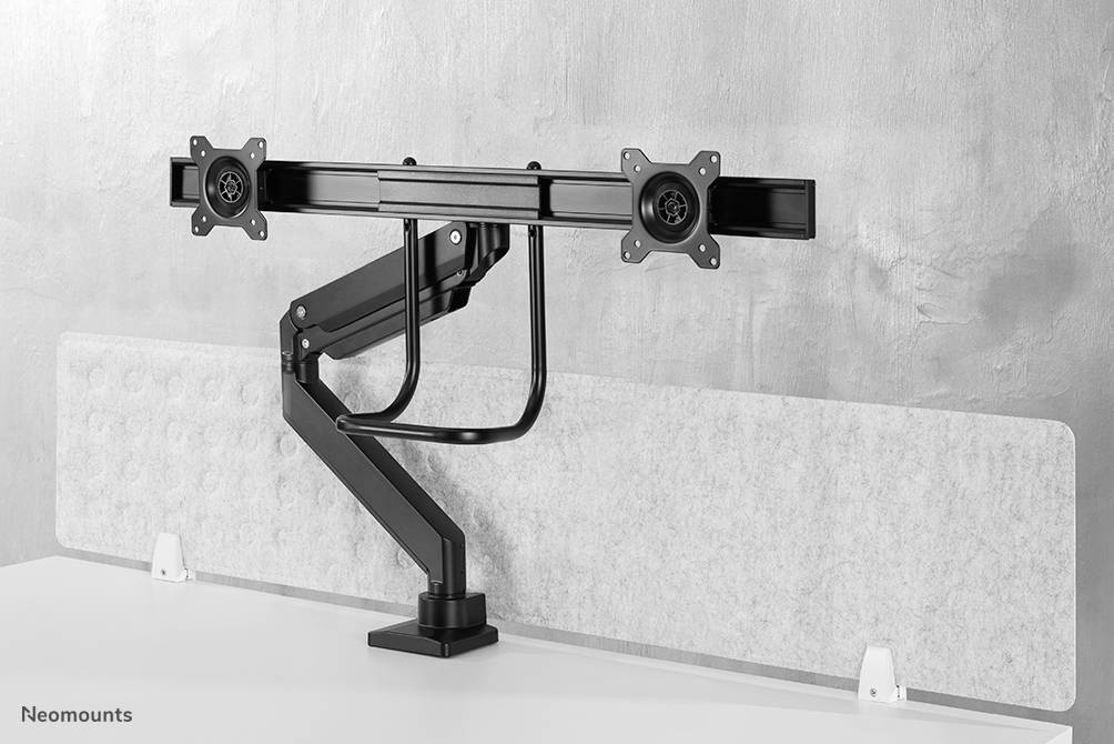 Doppel-Monitorhalterung mit zwei beweglichen Armen auf weißem Tisch, vor einer grauen Wand montiert.