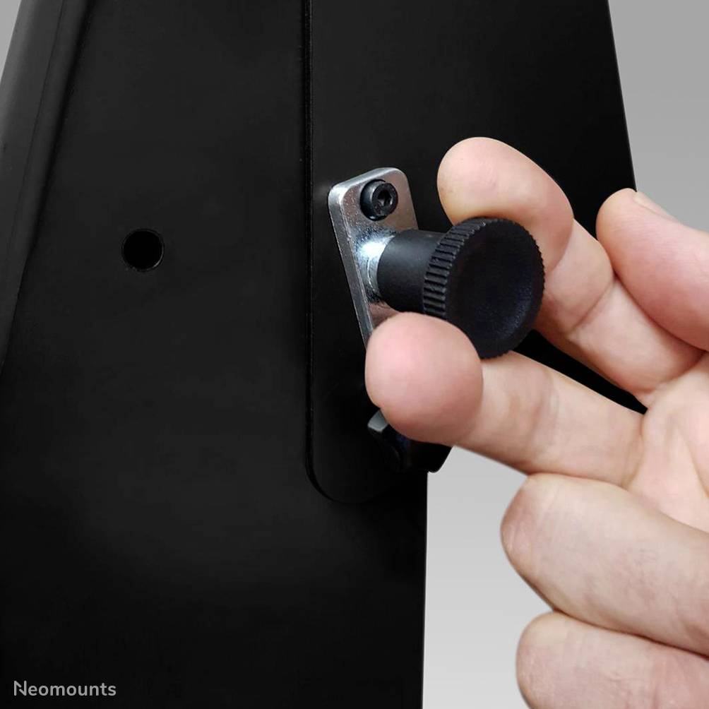 Hand dreht einen schwarzen Knopf an der Rückseite eines Monitors, wahrscheinlich zur Anpassung oder Befestigung.