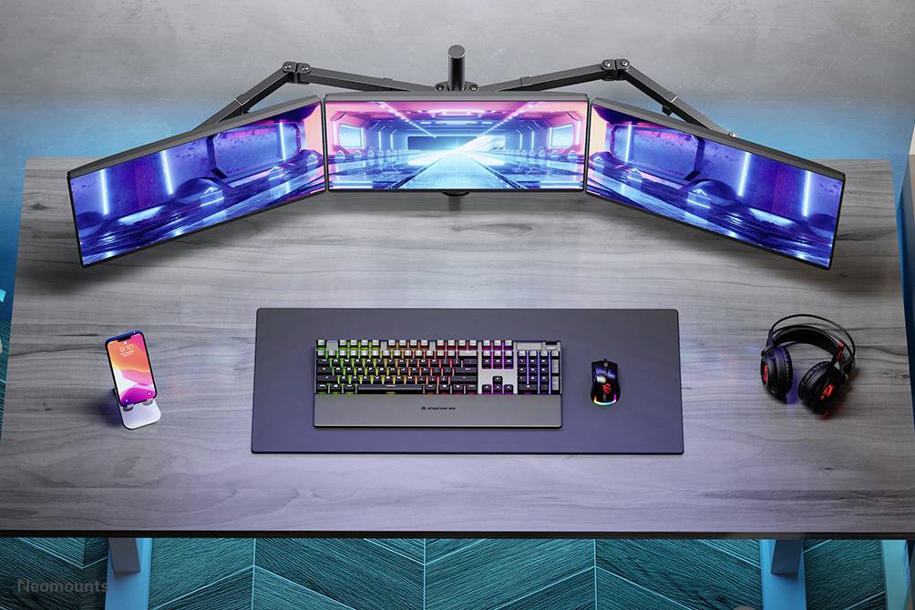 Ein moderner Schreibtisch mit Tastatur, Maus, Smartphone, Kopfhörern und drei gebogenen Monitoren, die ein futuristisches blau-pinkes Bild zeigen.