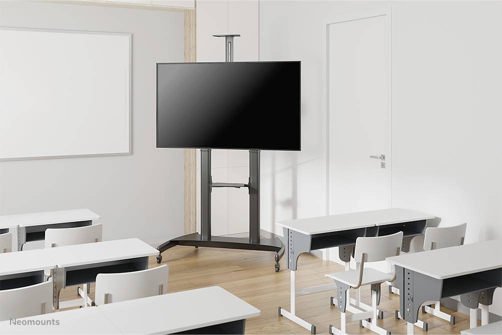 Ein leerer Klassenraum mit weißen Tischen und Stühlen. Ein großer, schwarzer Bildschirm auf einem Rollständer steht vorne neben einer geschlossenen Tür.