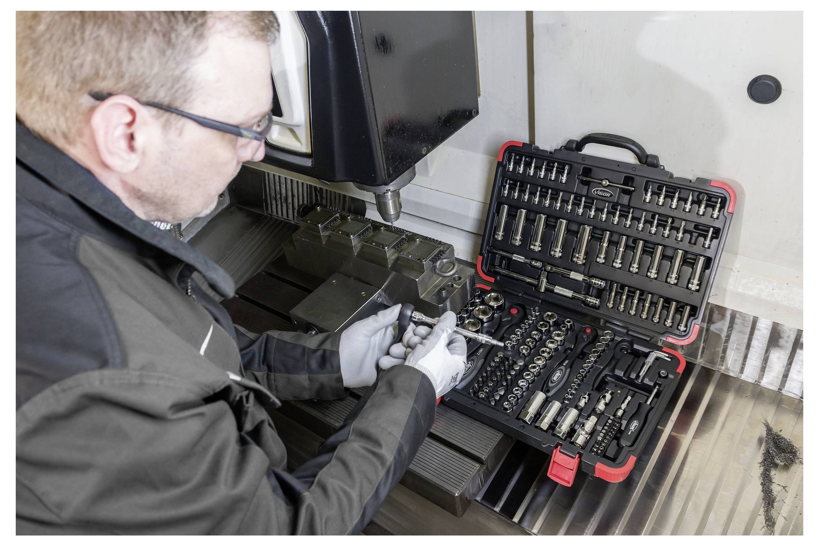 Techniker, der einen Steckschlüssel- und Schraubenschlüsselsatz verwendet, um an einer Metallmaschine in einer industriellen Werkstatt zu arbeiten.