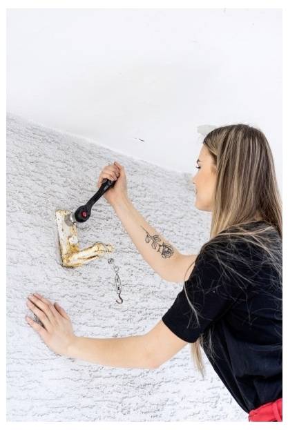Frau, die einen Ratschenschlüssel verwendet, um eine an der Wand montierte Metallhalterung an einer strukturierten weißen Wand anzuziehen oder zu lockern.