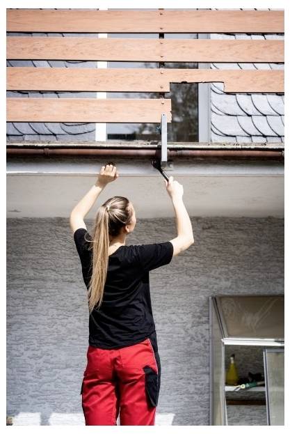 Person auf einer Leiter repariert das Dach und ersetzt hölzerne Latten über einer Hauswand.