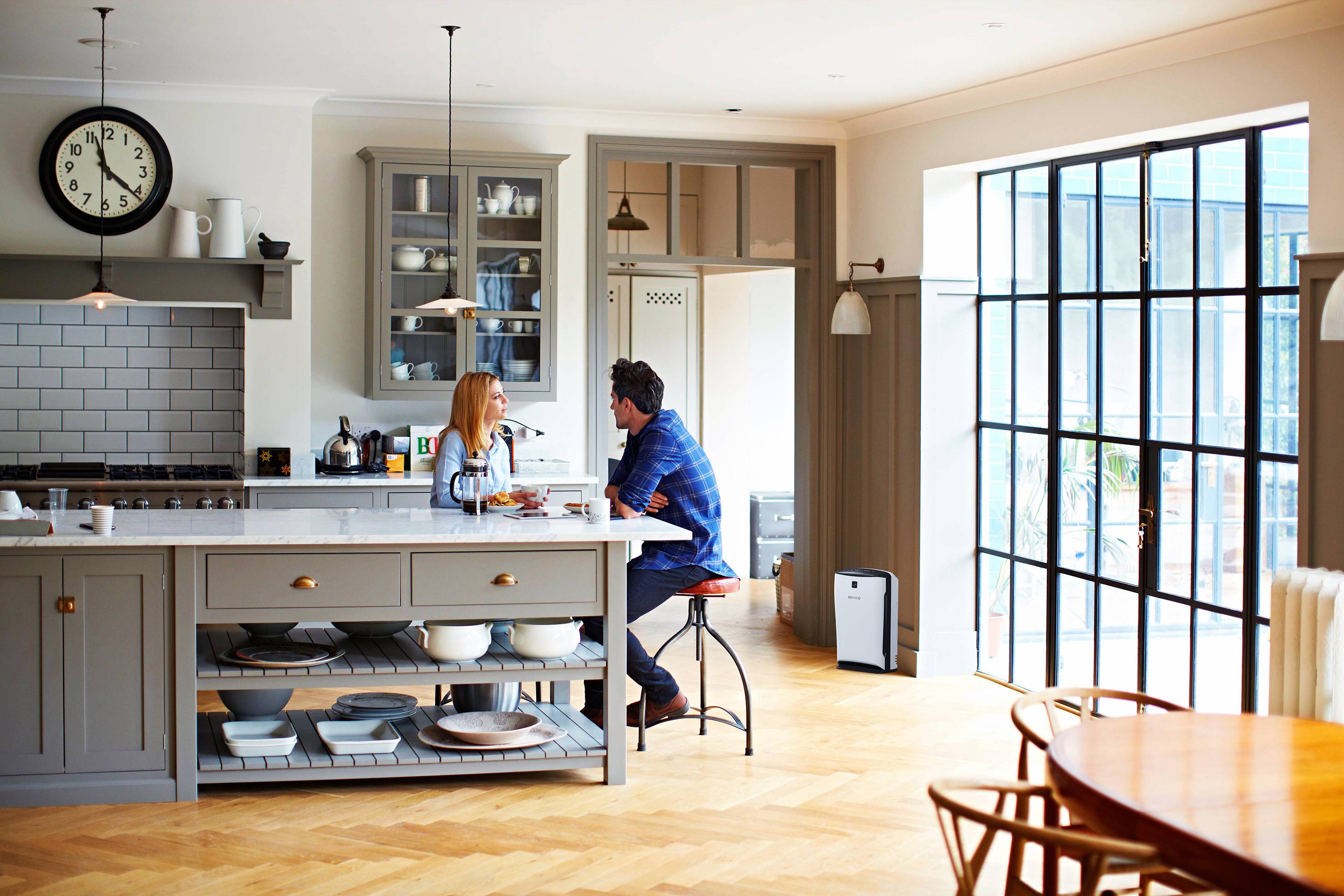 Eine moderne Küche mit einem großen Fenster. Zwei Personen sitzen am Küchentresen und unterhalten sich.