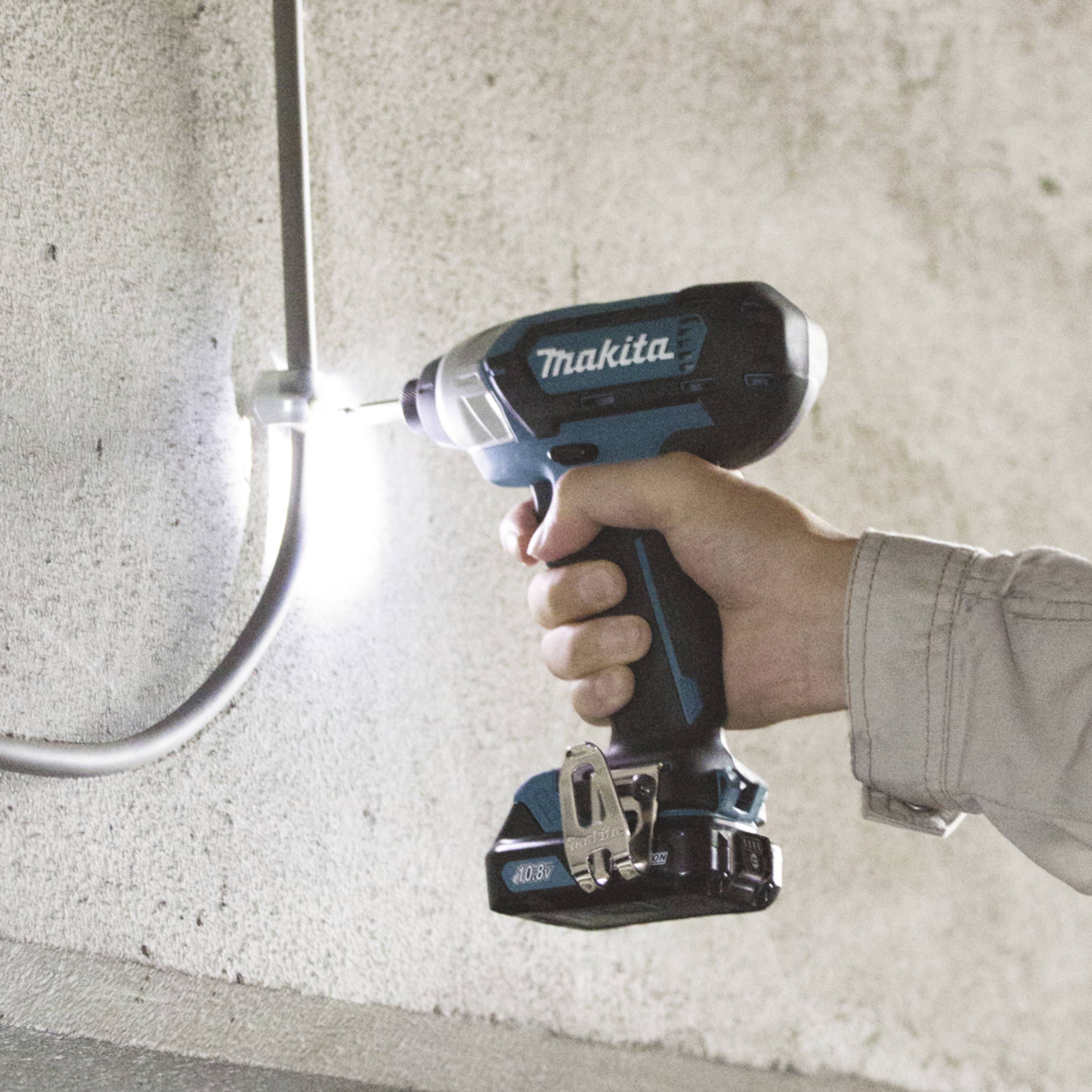 Eine Person benutzt einen blauen Akkuschrauber, um eine Schraube in eine Wand zu drehen. Ein graues Kabel verläuft parallel zur Wand.