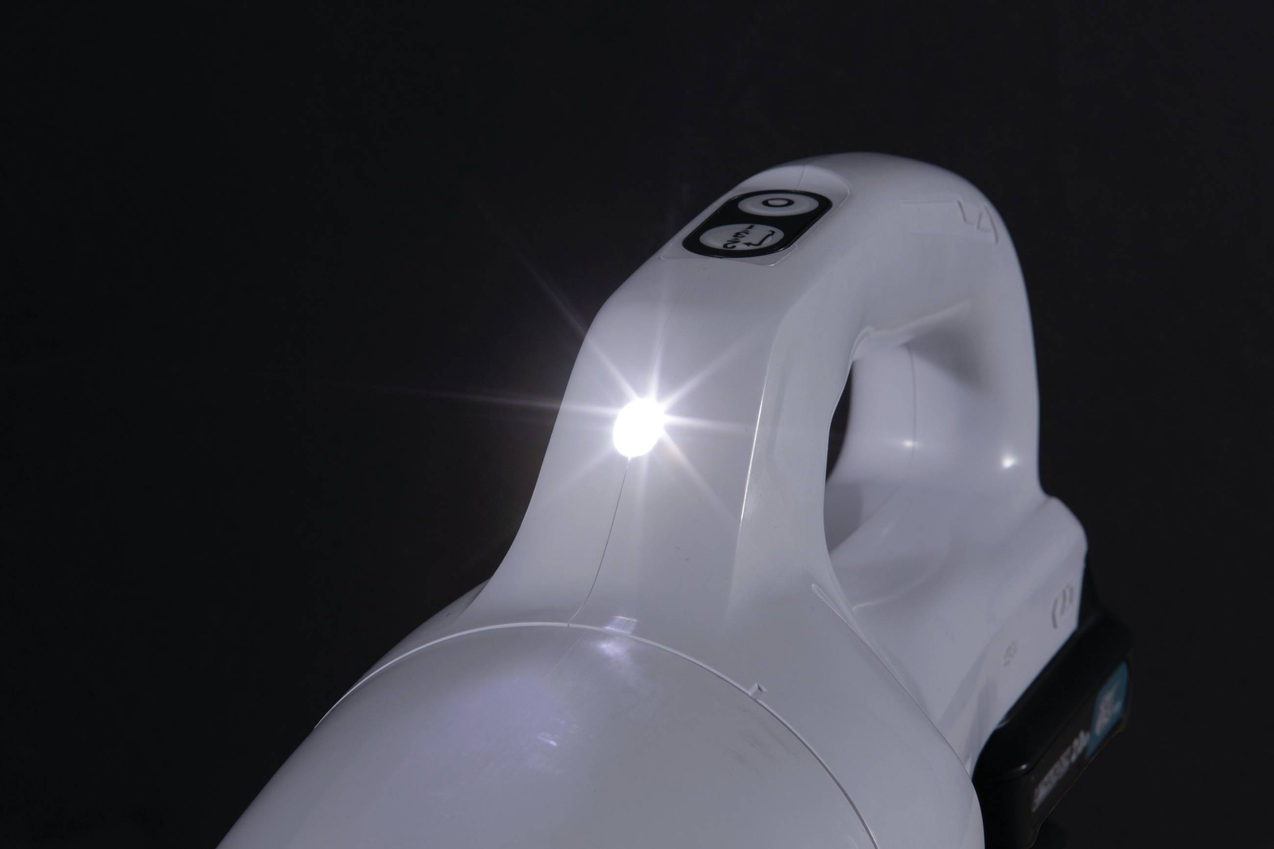 Ein weißer Akku-Staubsauger mit eingeschaltetem LED-Licht. Der Hintergrund ist dunkel, wodurch das Licht gut sichtbar ist.