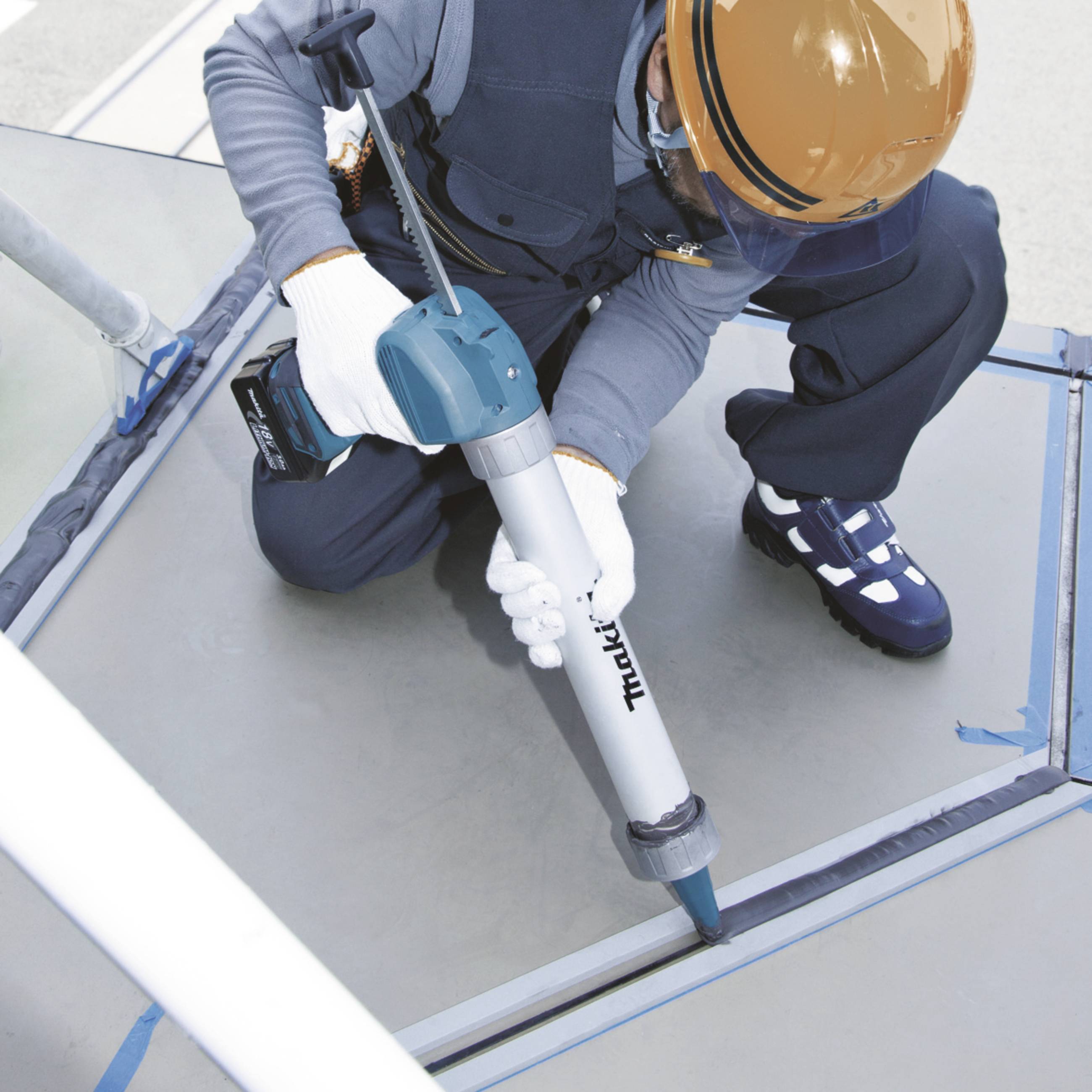 Eine Person auf einem Dach kniet und benutzt ein elektrisches Werkzeug zum Versiegeln von Fugen. Sie trägt Schutzkleidung und einen Helm.