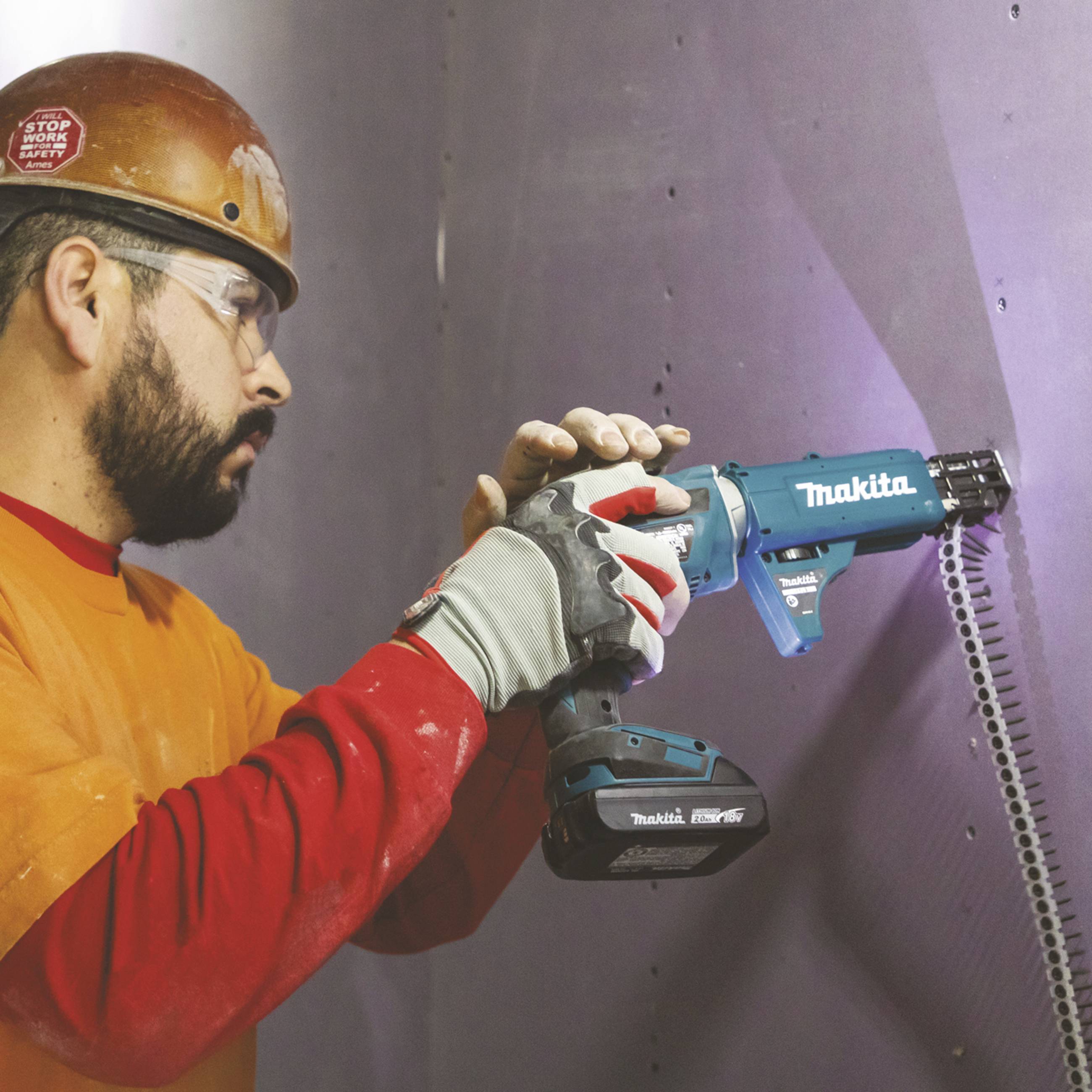 Eine Person in Arbeitskleidung verwendet ein elektrisches Werkzeug, um eine Schraube in die Wand zu bohren.