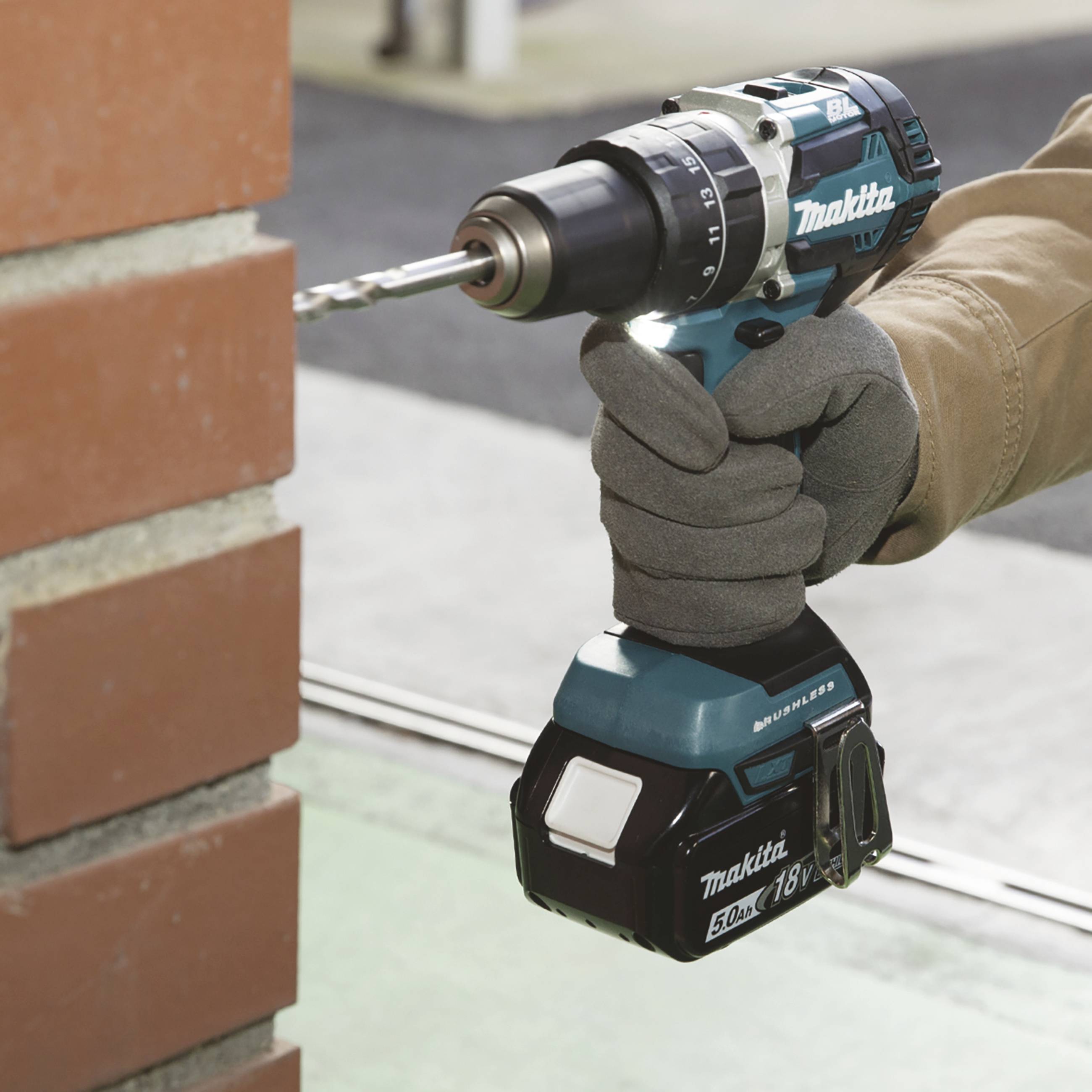 Eine Person in Arbeitshandschuhen benutzt eine blaue Akku-Bohrmaschine, um ein Loch in eine rote Ziegelwand zu bohren.