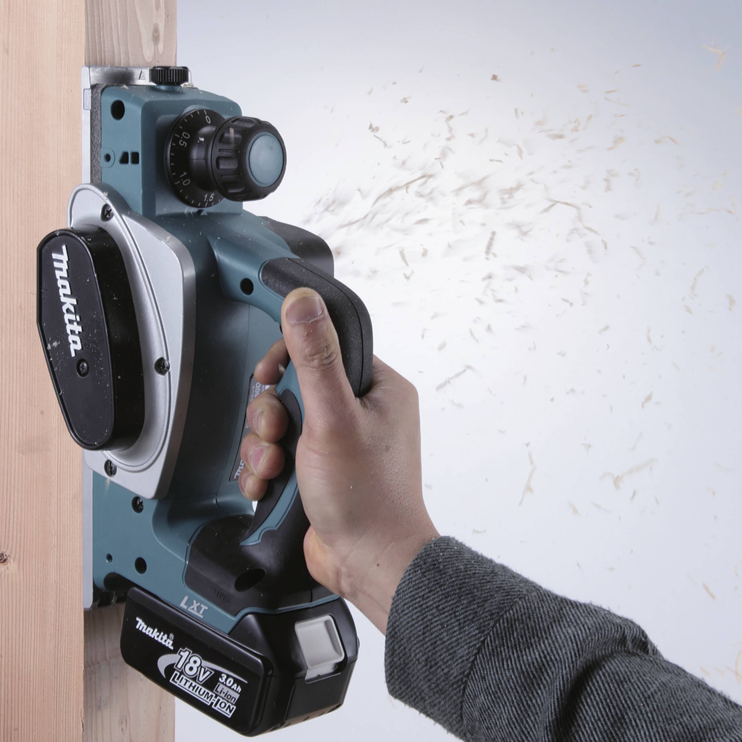 Eine Person verwendet einen kabellosen Makita-Handhobel, um Holzspäne von einem Holzbrett zu entfernen.