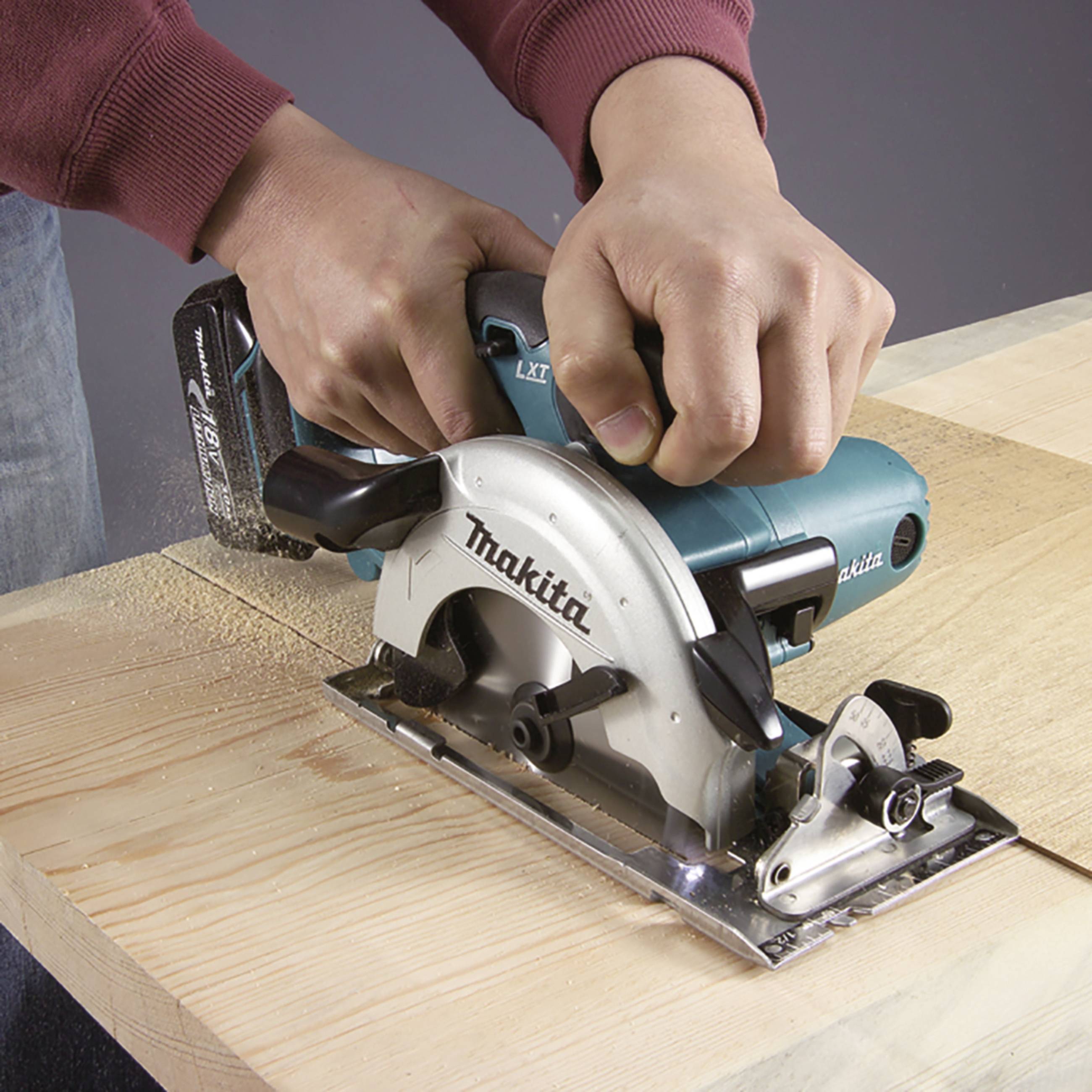 Eine Person sägt mit einer blauen elektrischen Handkreissäge auf einem Holzbrett. Die Säge trägt die Aufschrift 'Makita'.