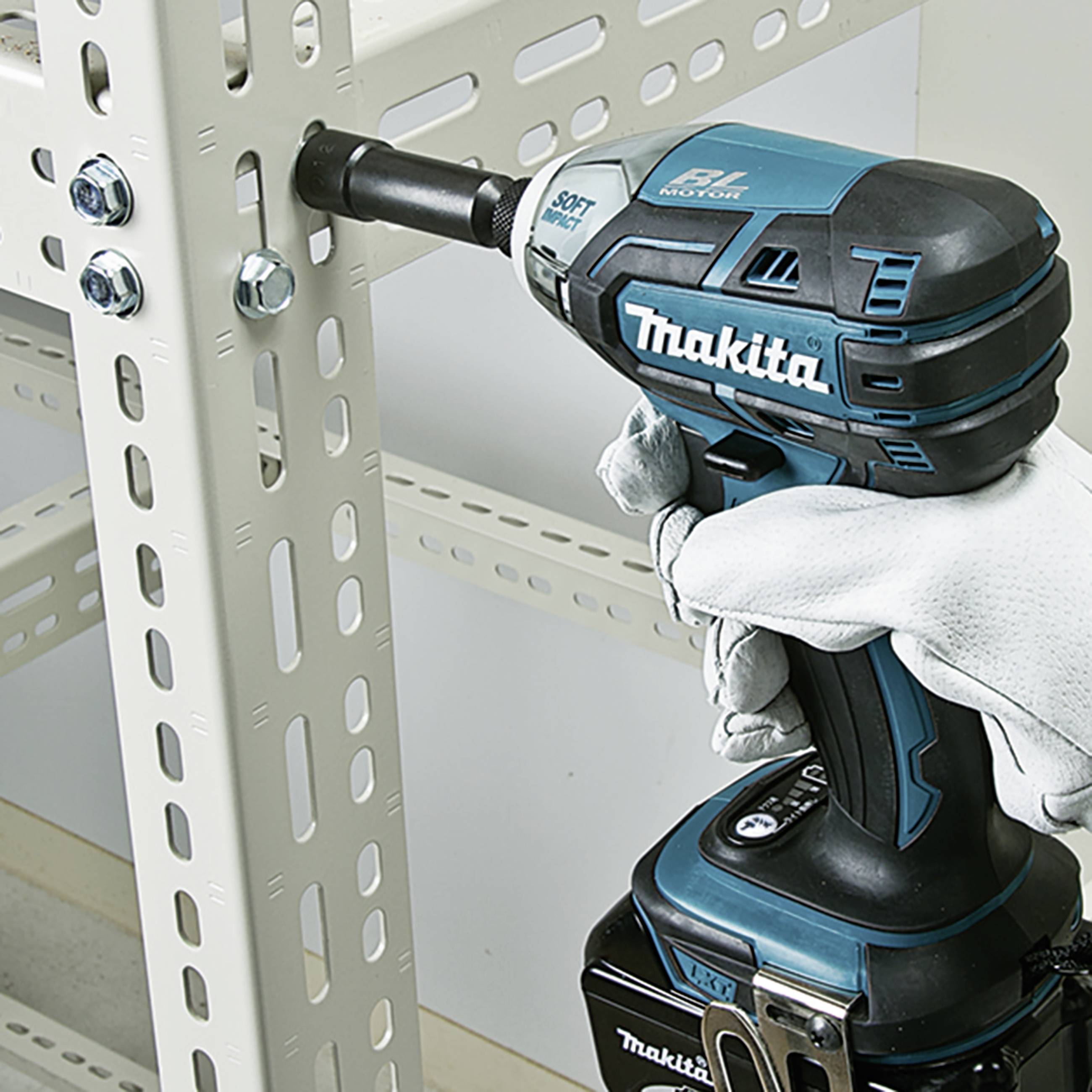 Akkubohrschrauber der Marke Makita zieht eine Schraube in ein Metallregal ein. Eine Person in Arbeitshandschuhen hält das Gerät fest.