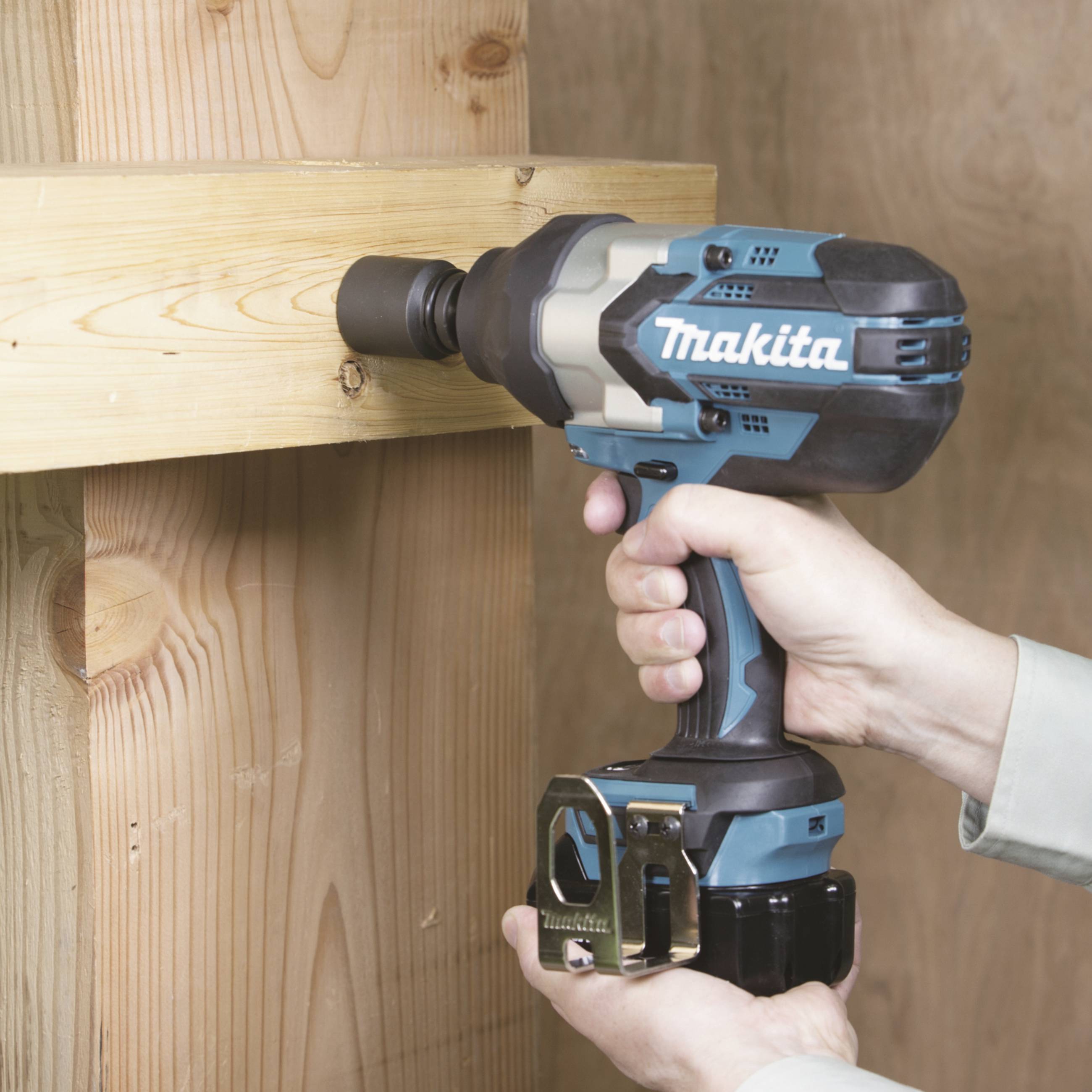 Eine Person verwendet eine blaue Bohrmaschine, um eine Schraube in ein Holzbalken einzuschrauben. Die Marke der Bohrmaschine ist sichtbar.