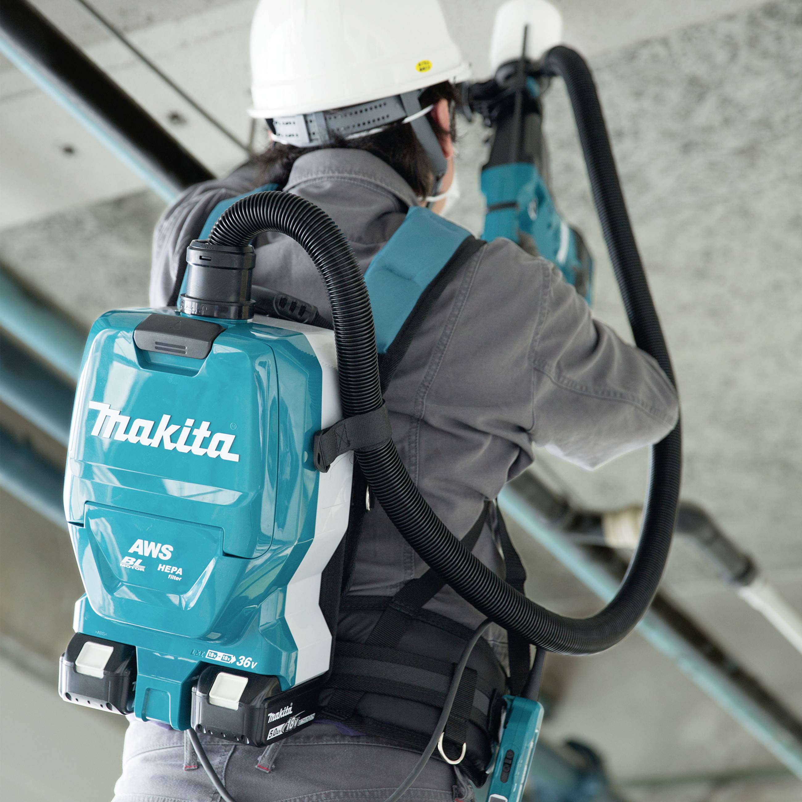 Eine Person trägt einen Makita-Akkusauger auf dem Rücken und reinigt ein Rohr in einem industriellen Umfeld.