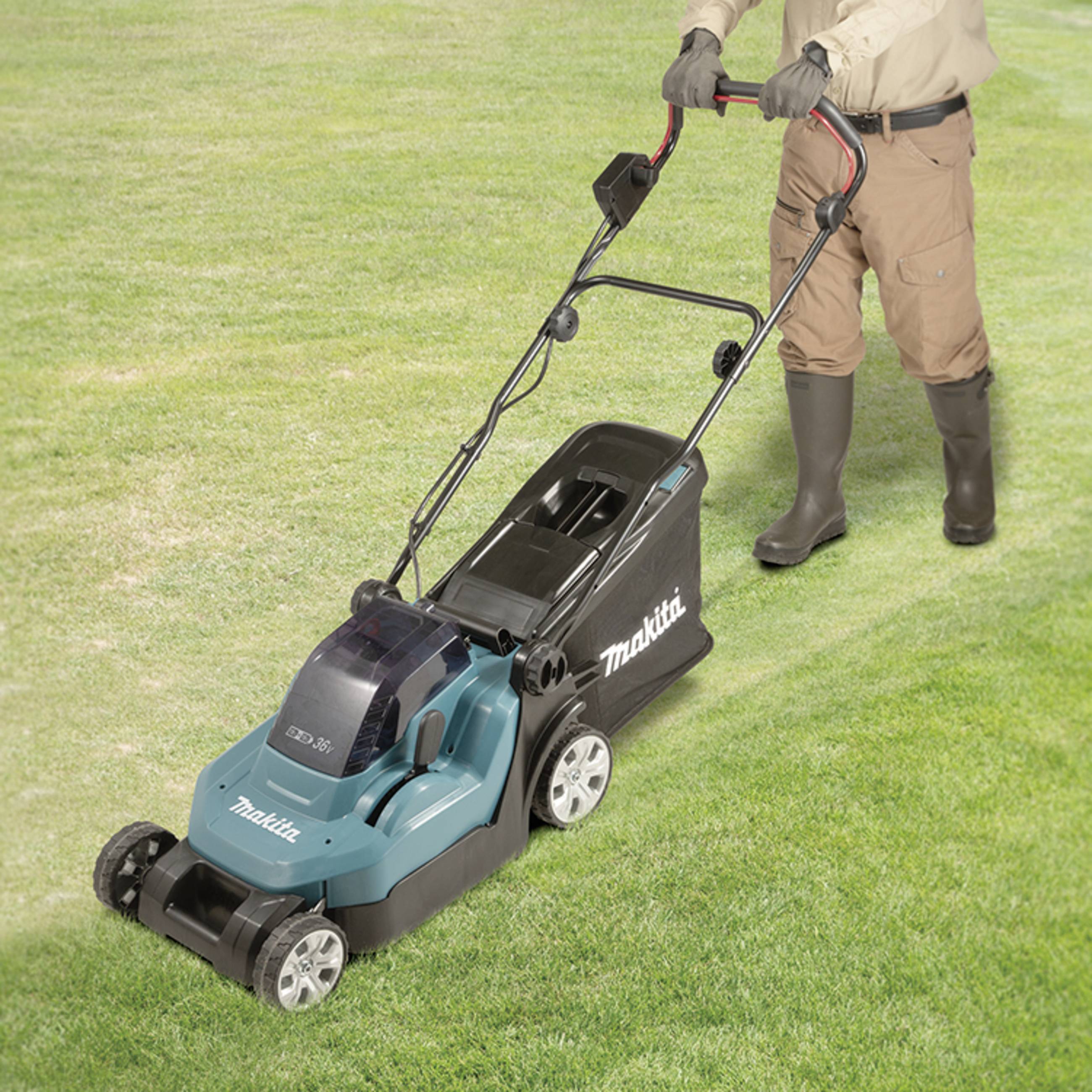 Eine Person mäht den Rasen mit einem blauen elektrischen Rasenmäher auf grünem Gras. Die Person trägt Stiefel und Handschuhe.
