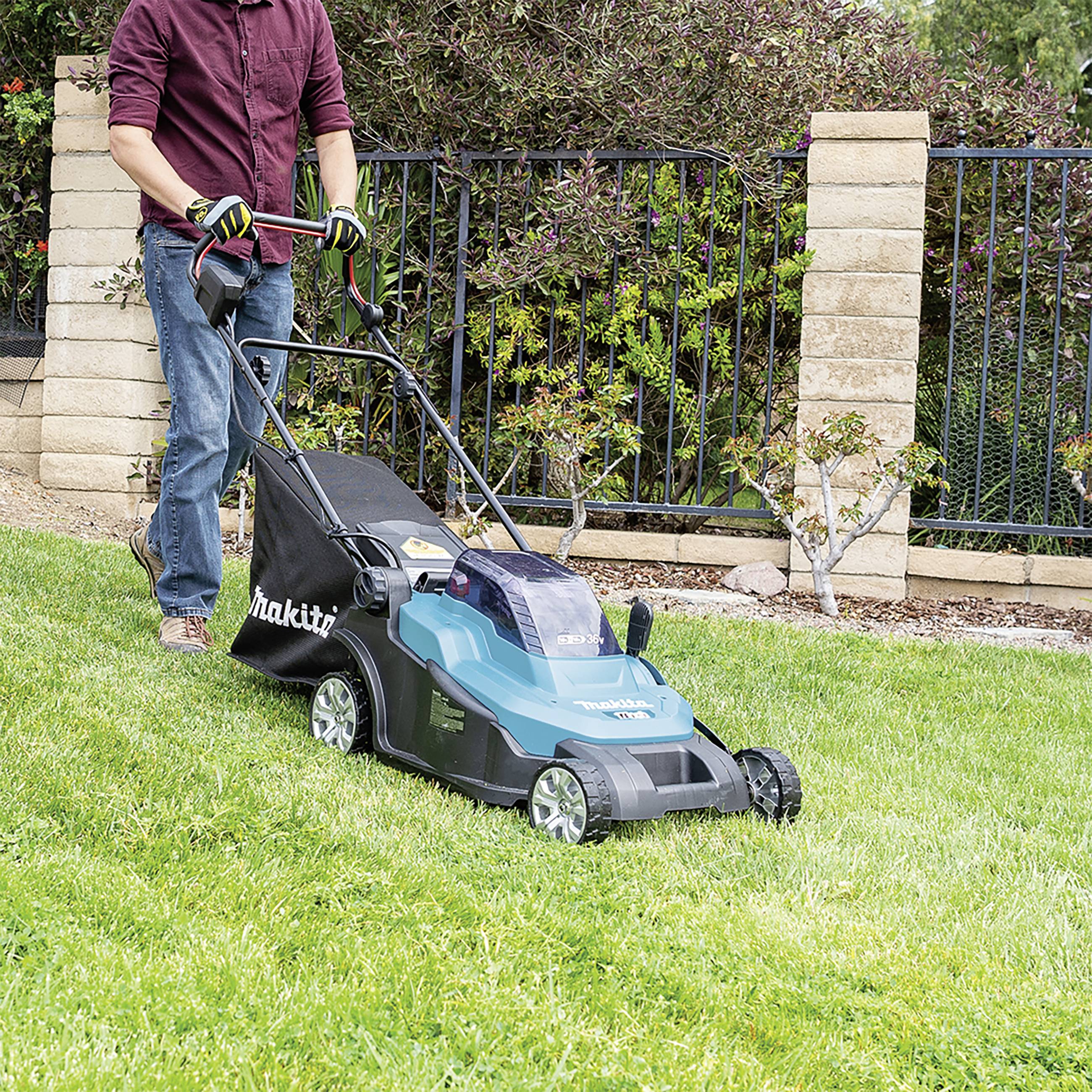 Eine Person mäht den Rasen mit einem elektrischen Rasenmäher auf einer grünen Wiese.