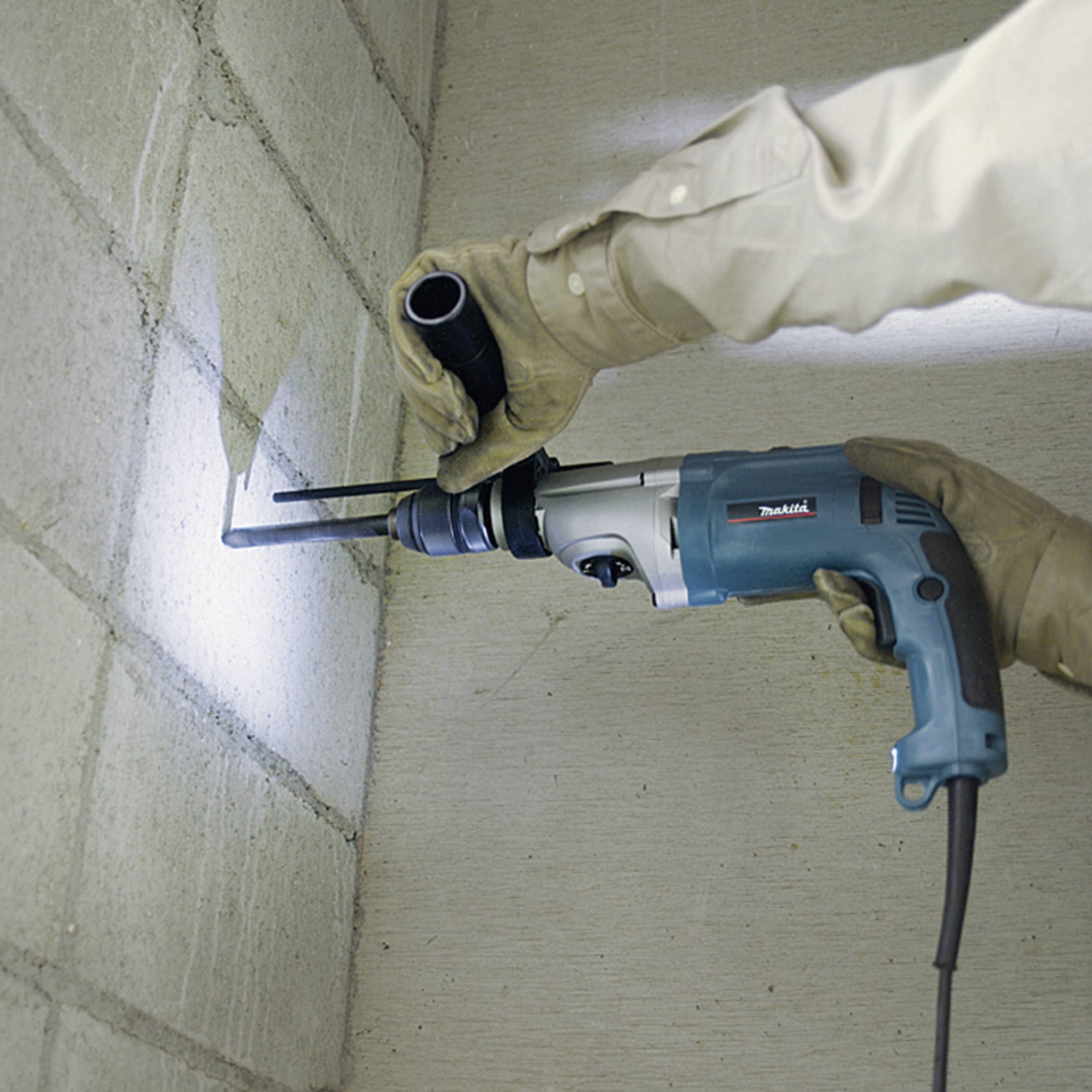Eine Person in Schutzkleidung bohrt mit einer elektrischen Bohrmaschine ein Loch in eine Ziegelwand.