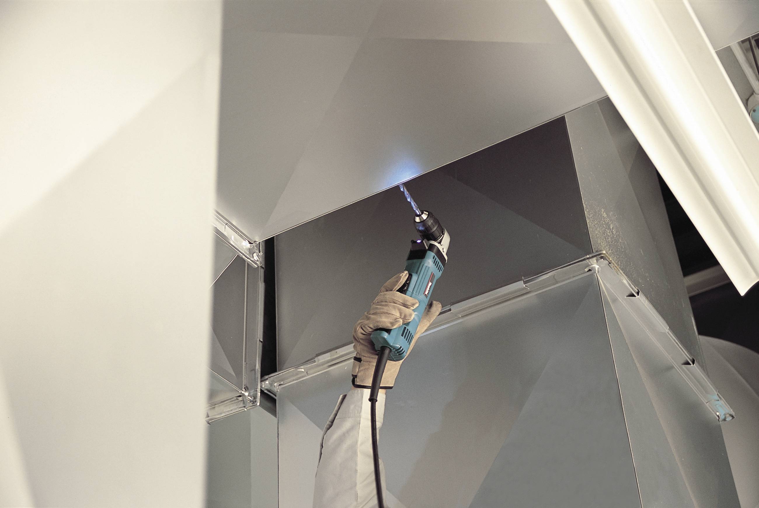 Eine Person schützt mit Handschuhen Lüftungsrohre, indem sie mit einem Gasbrenner die Kante erhitzt. Die Umgebung wirkt industriell.