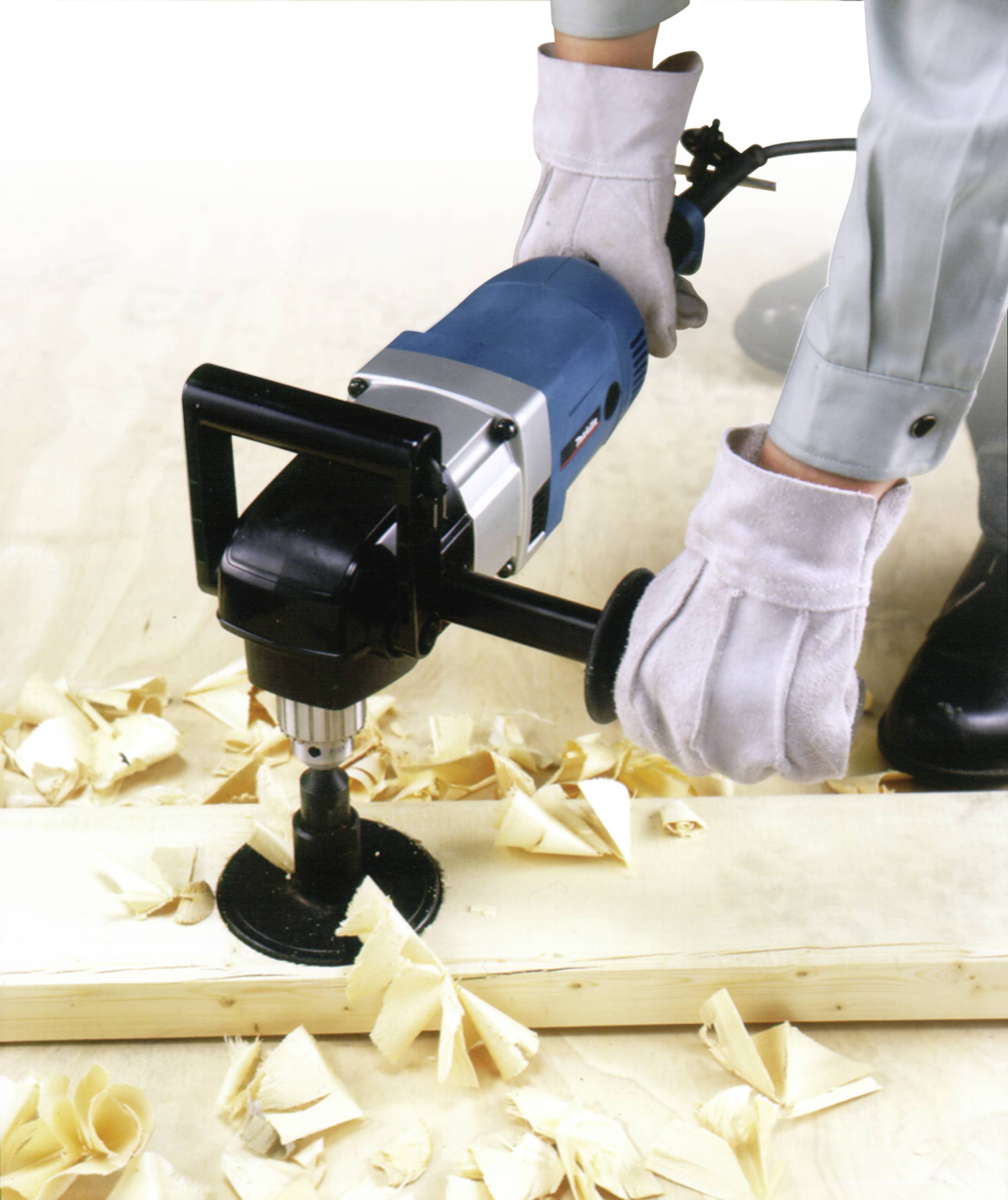 Eine Person bearbeitet ein Holzbrett mit einem elektrischen Bohrwerkzeug, Späne sind um das Werkstück verstreut.