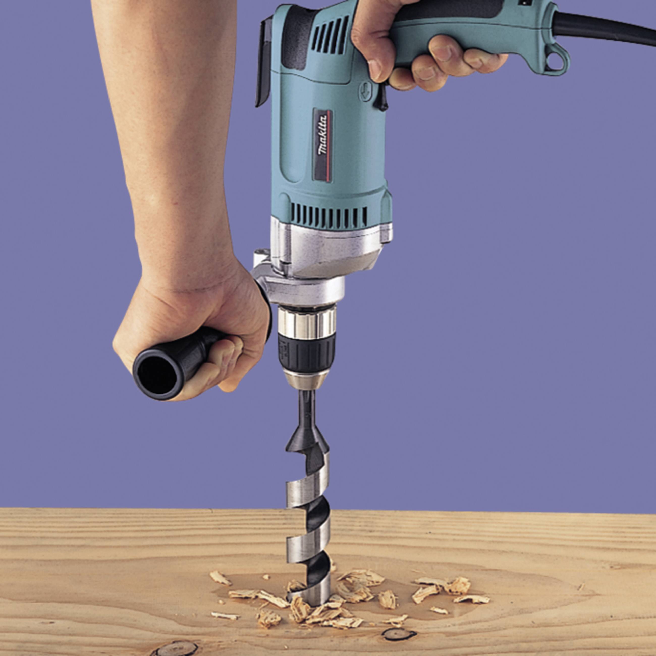 Eine Hand hält einen Bohrer, der in ein Holzbrett bohrt. Holzspäne sind um das Bohrloch verteilt, Werkstatt-Umgebung.