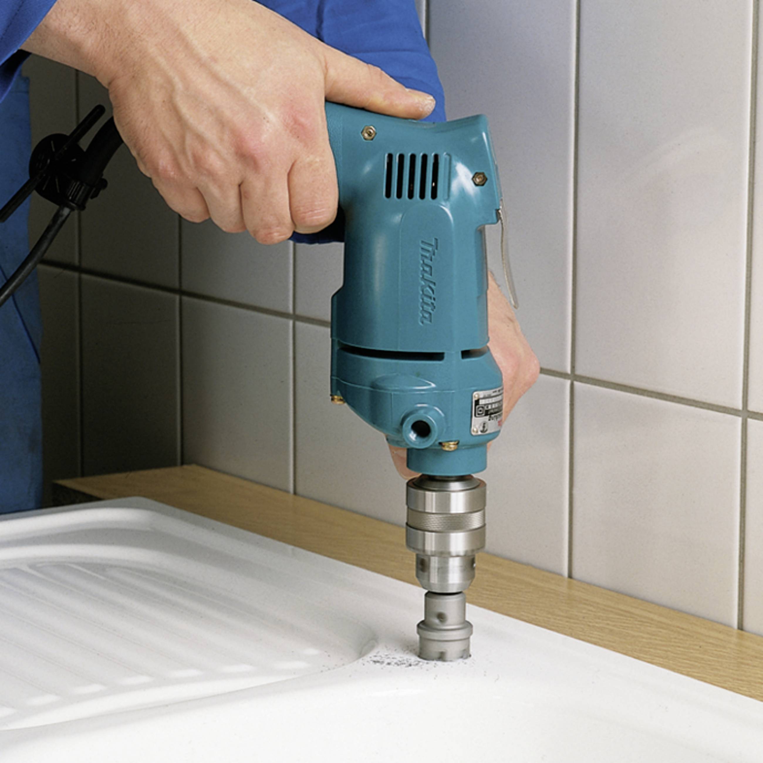 Eine Person bohrt mit einer blauen Bohrmaschine ein Loch in eine weiße Oberfläche, möglicherweise, um einen Wasserhahn zu montieren.