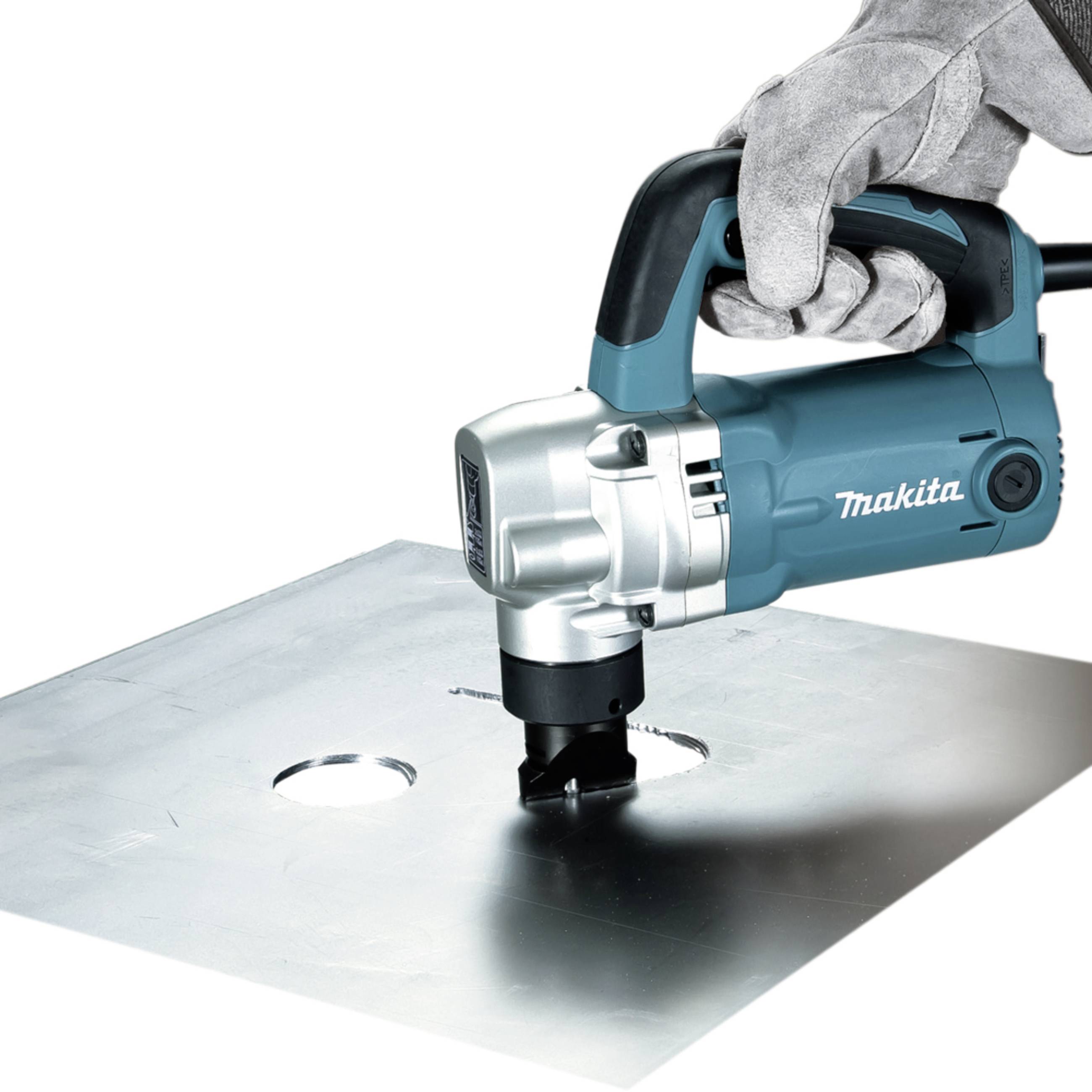 Eine Person mit Handschuhen benutzt eine Makita-Metallschneidmaschine, um präzise Löcher in ein großes Metallblech zu schneiden.