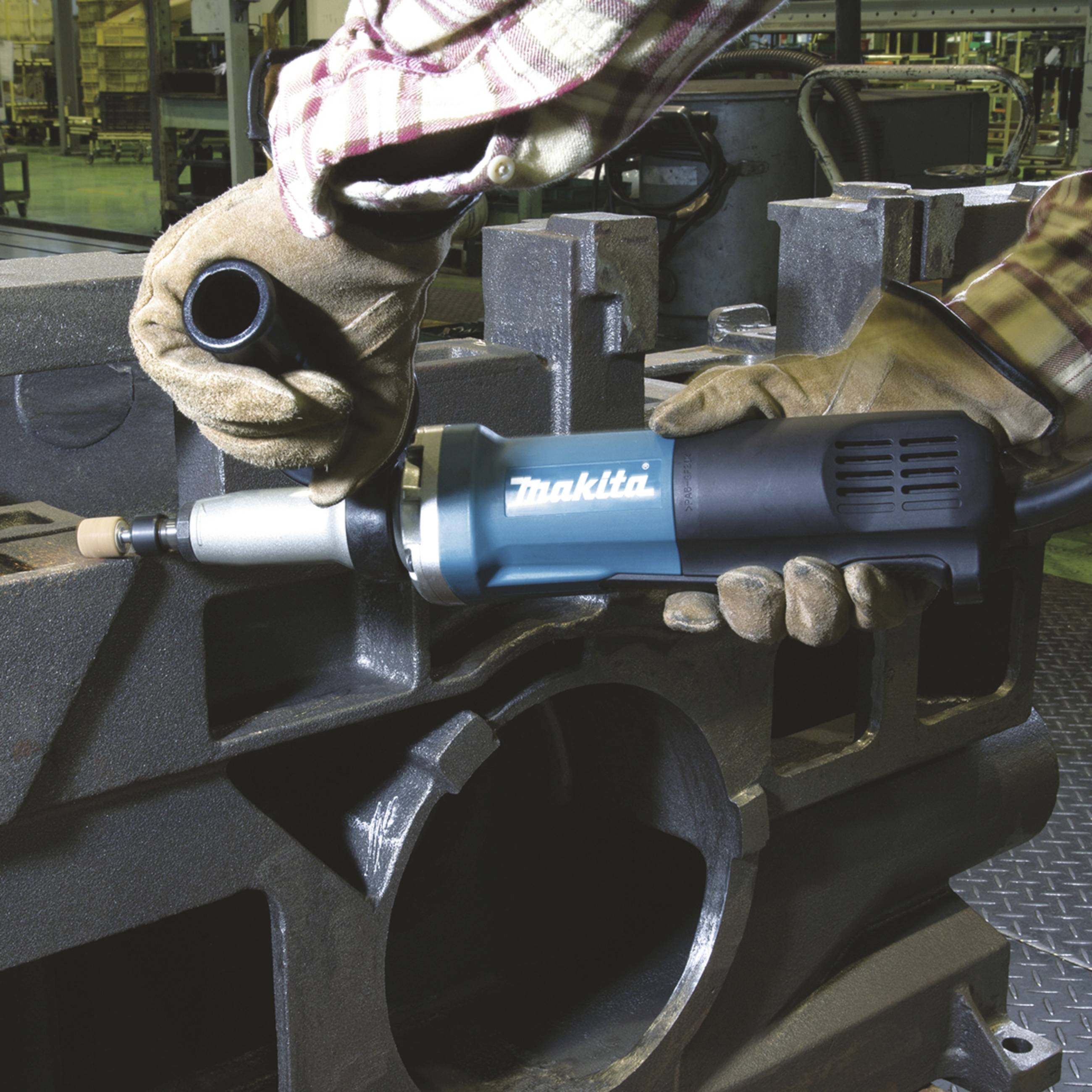 Eine Person in Arbeitskleidung verwendet ein elektrisches Schleifwerkzeug, um Metall in einer Werkstattumgebung zu bearbeiten.