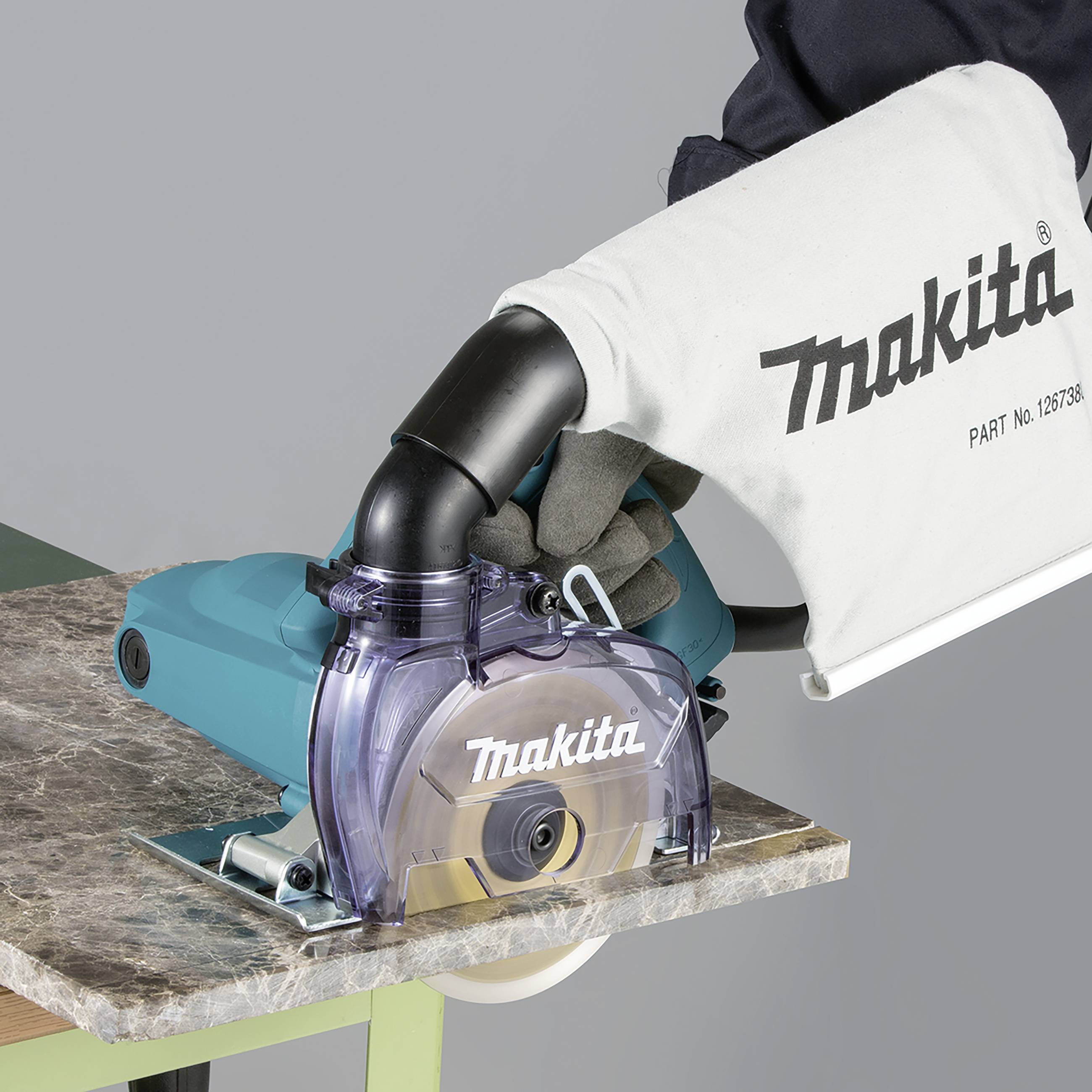 Eine Hand hält eine Makita-Kreissäge mit Staubsack, die auf einem Holztisch positioniert ist.