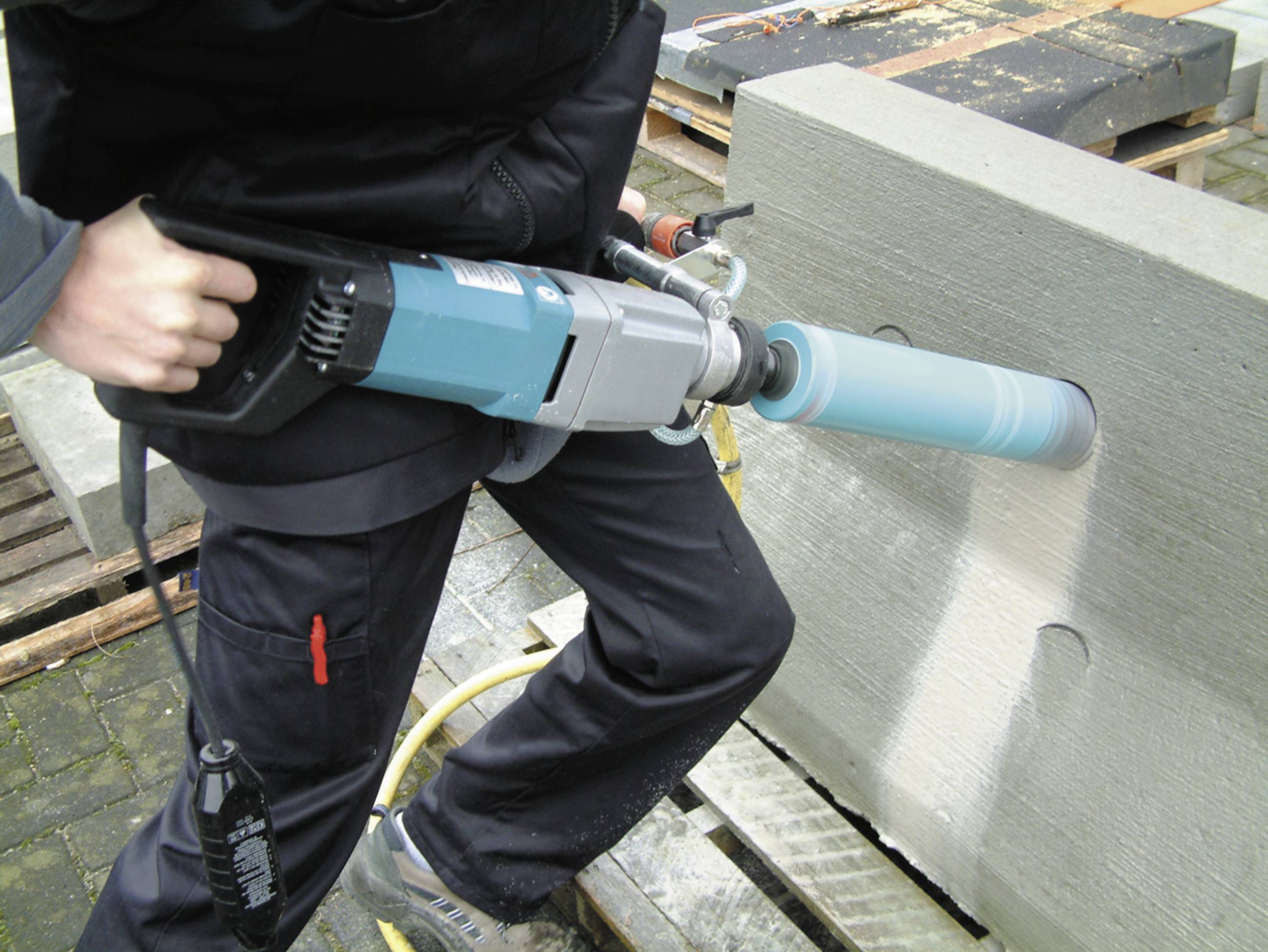Person verwendet einen Bohrhammer, um ein rundes Loch in einen Betonblock zu bohren.