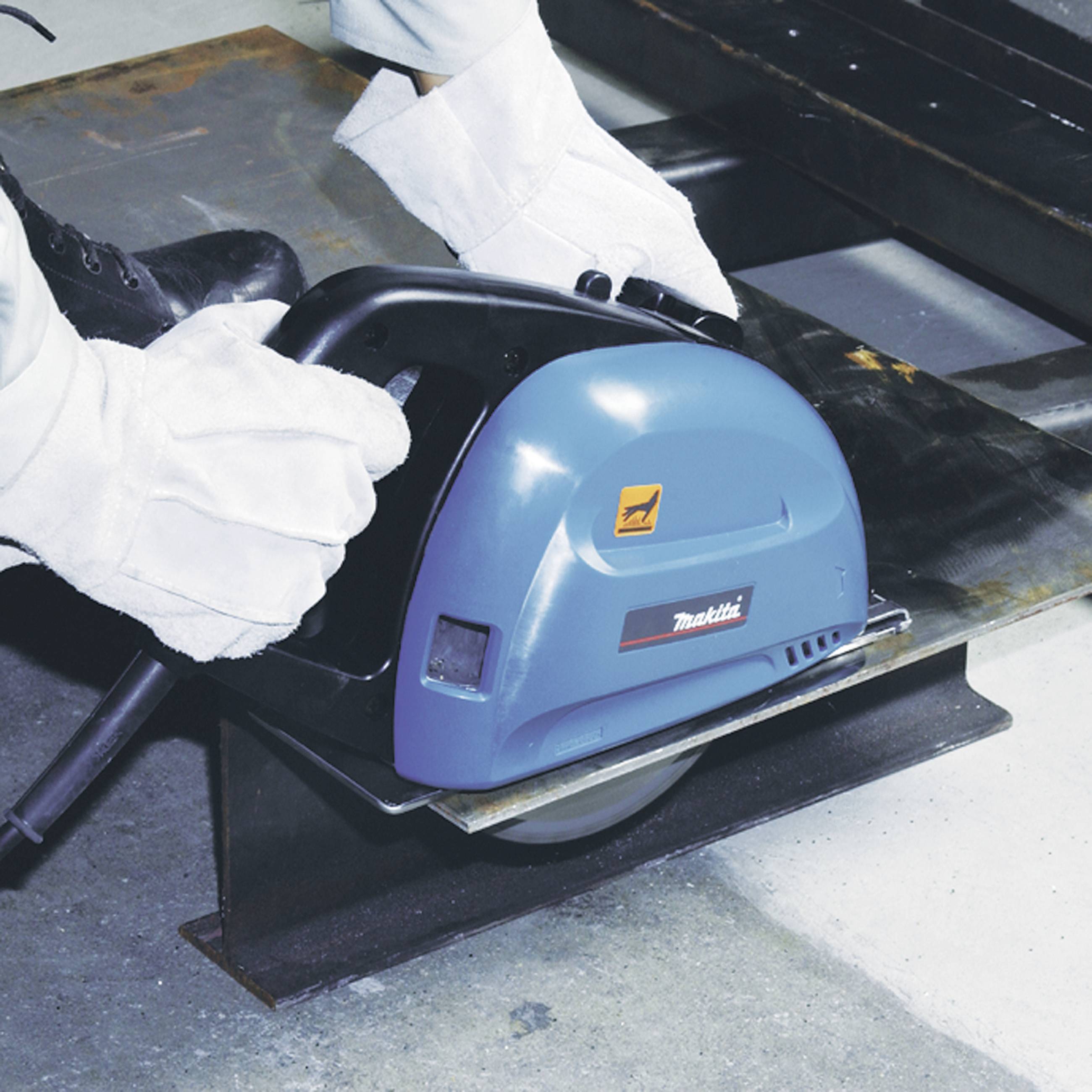 Eine Person schneidet Metall mit einer blauen Industriesäge in einer Werkstatt. Fokus liegt auf der Präzision der Arbeit.