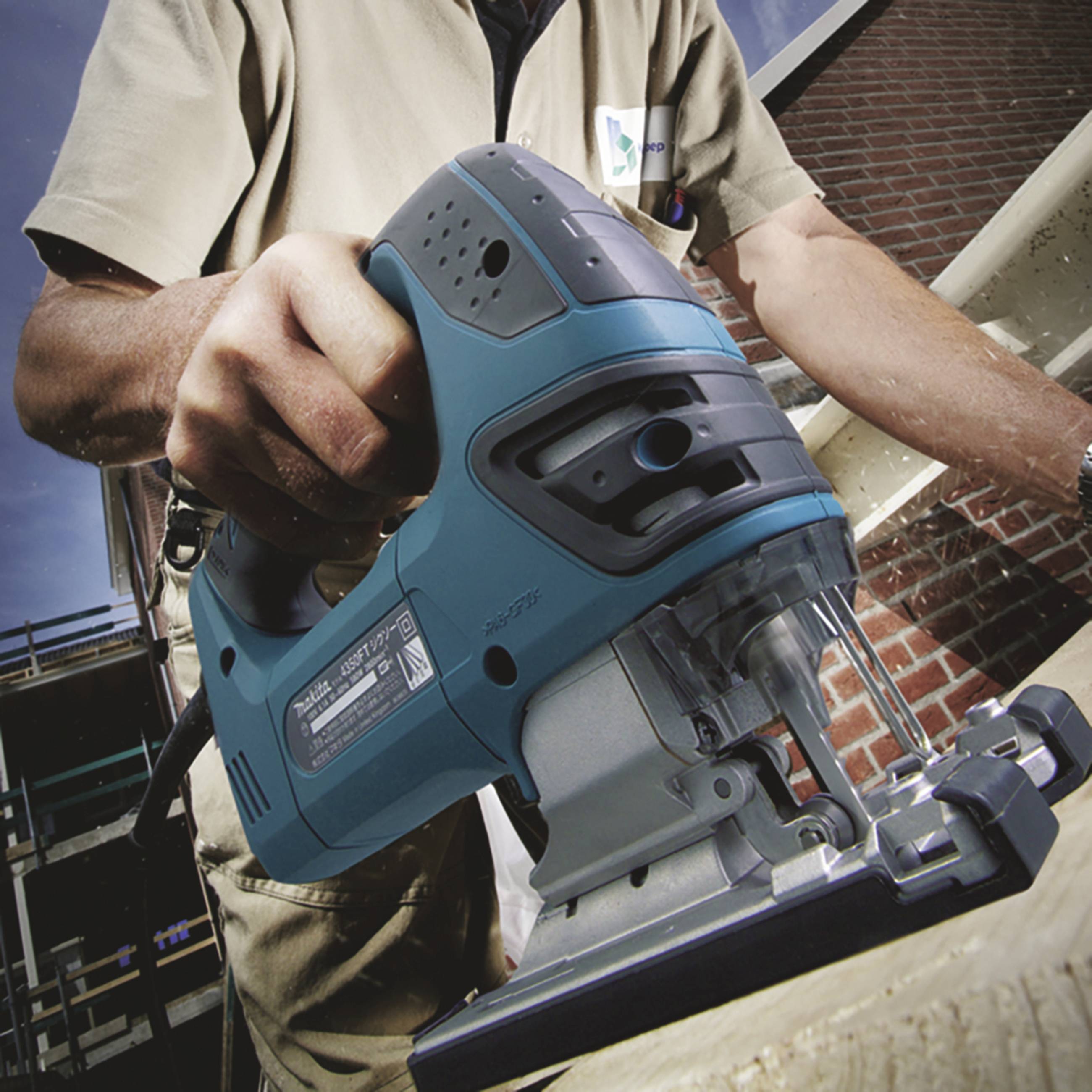 Eine Person hält eine elektrische Stichsäge und schneidet durch ein Holzbrett. Die Person trägt Arbeitskleidung.