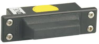 Ein rechteckiger, schwarzer Magnetsensor mit einem gelben Kreis oben, montiert auf einer flachen, grauen Oberfläche. Schrauben sind an den Ecken sichtbar.