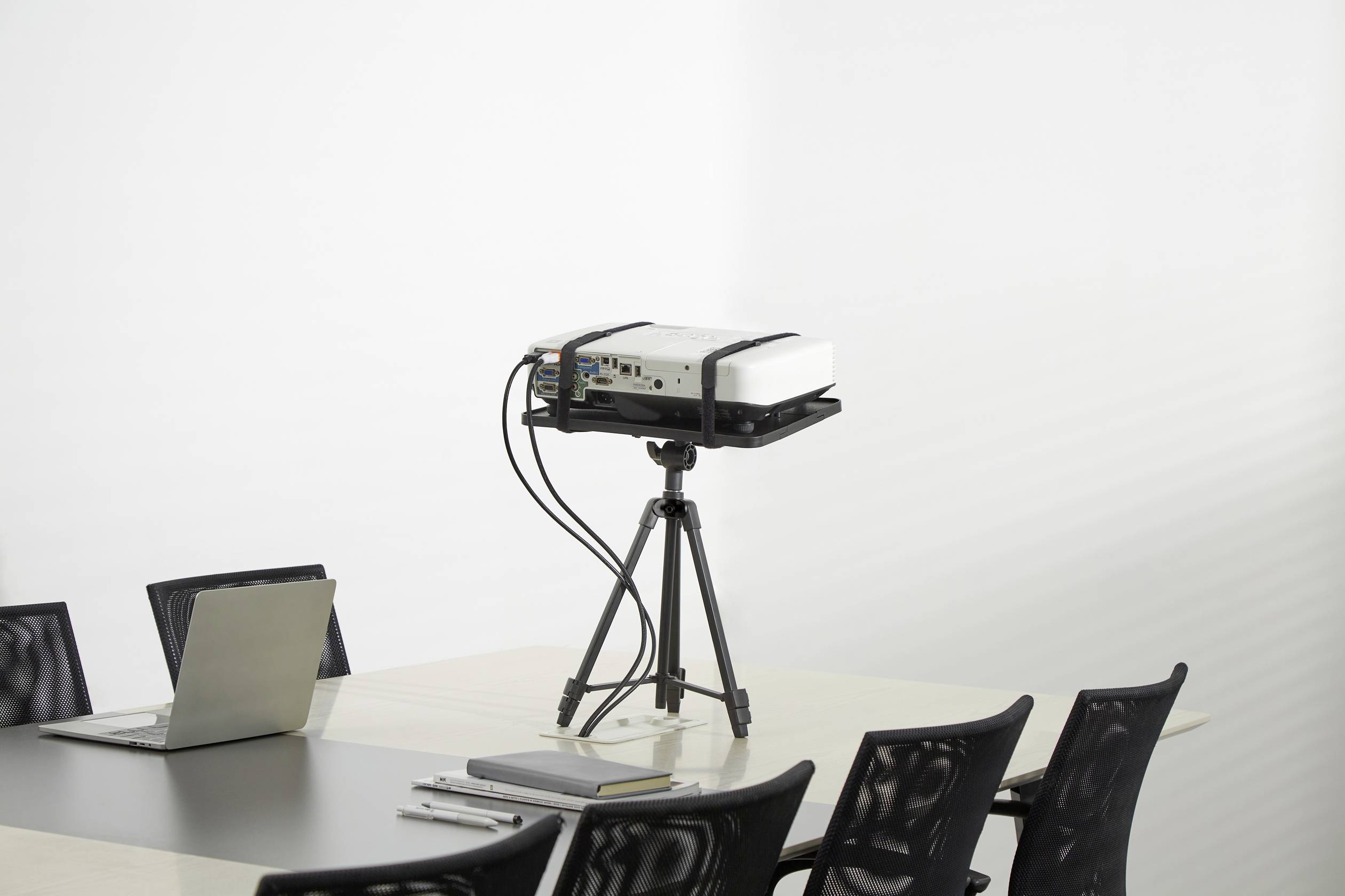 Ein Projektor steht auf einem Tisch in einem Konferenzraum, umgeben von mehreren leeren Stühlen und einem Laptop.