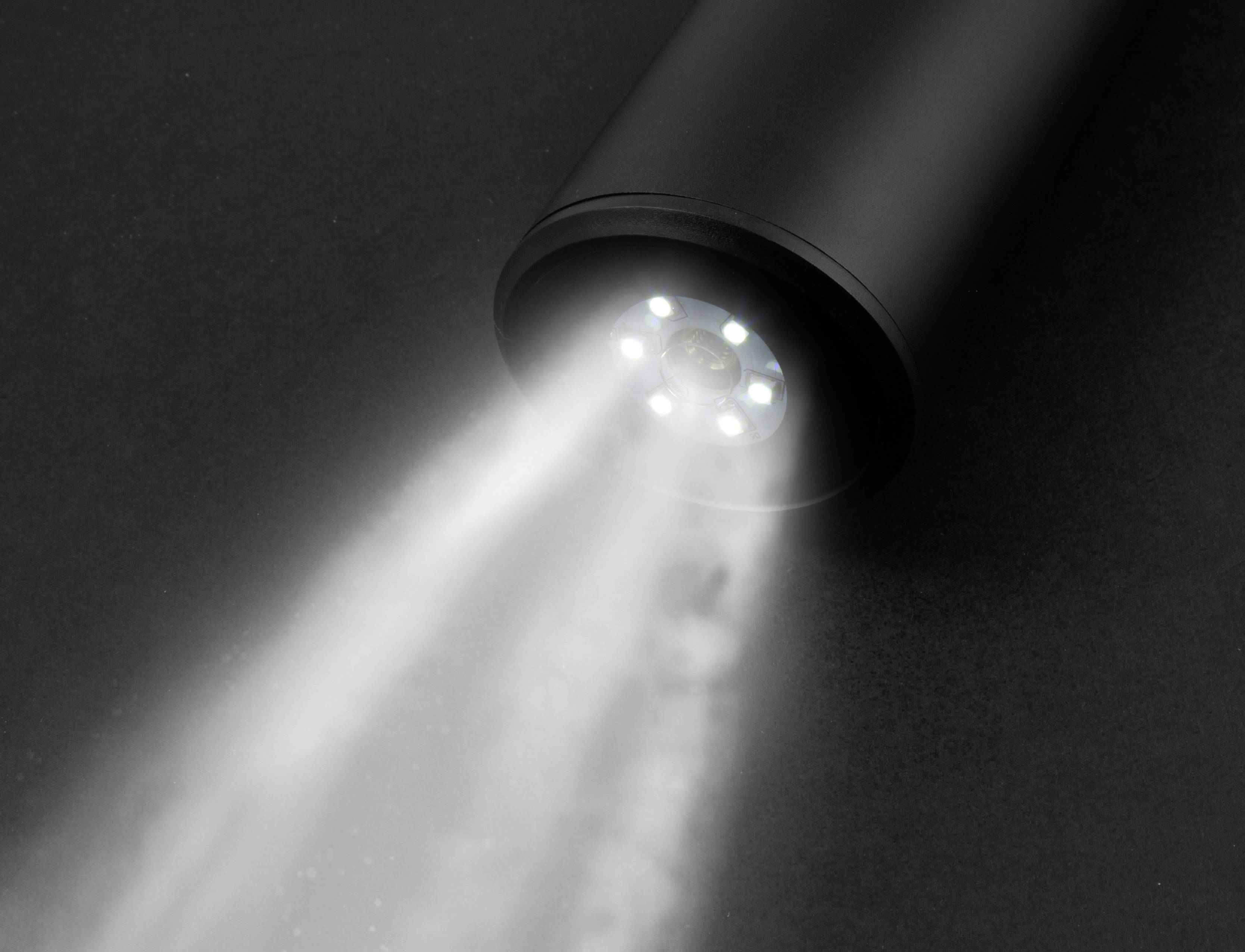 Nahaufnahme einer Taschenlampe, die einen hellen Lichtstrahl auf eine dunkle Oberfläche wirft.