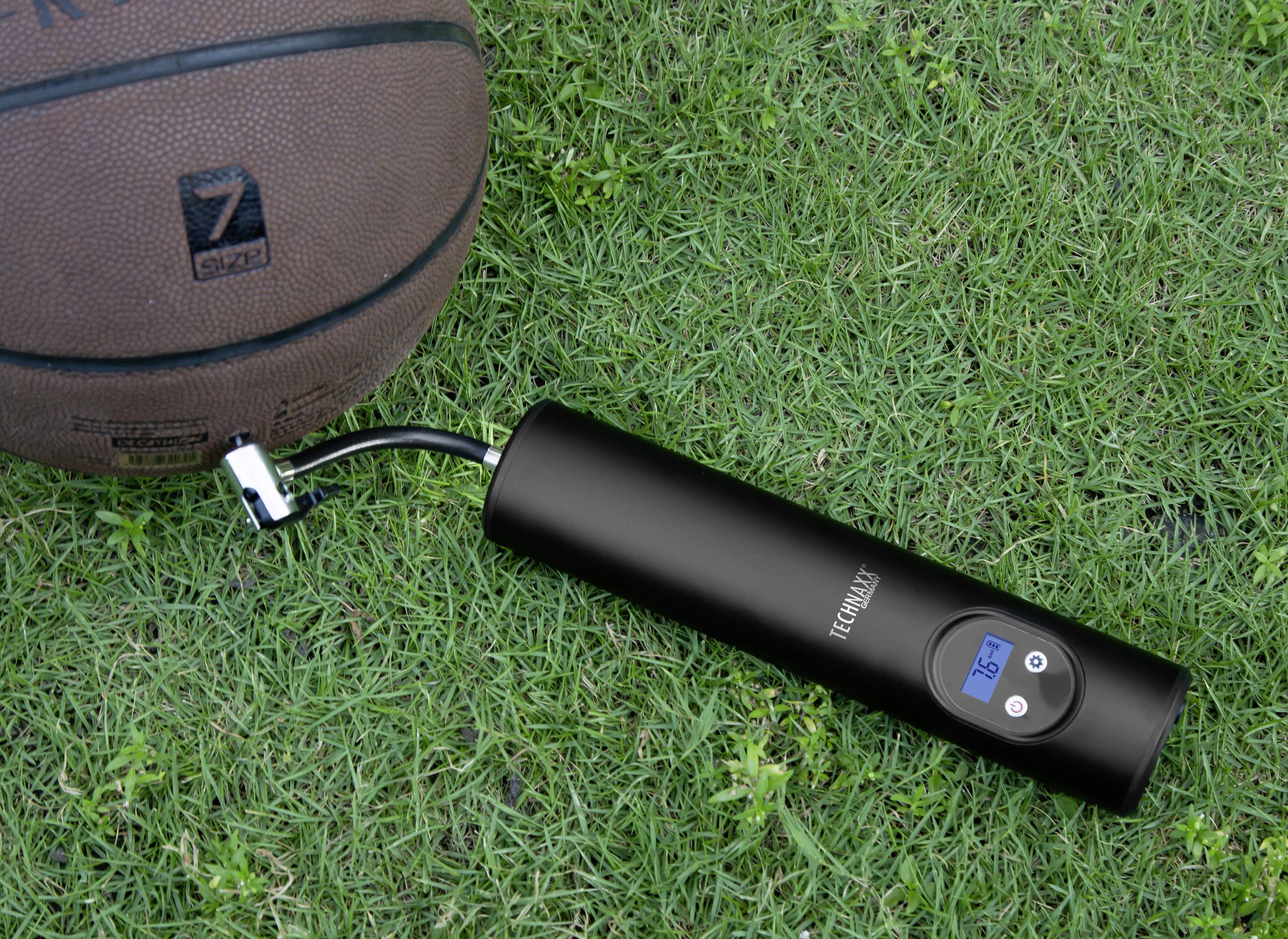 Ein Basketball liegt auf Gras neben einer schwarzen elektrischen Luftpumpe mit Digitalanzeige, die einen Druck von 3,5 bar zeigt.