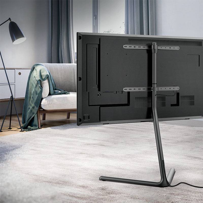 Ein Fernseher steht stilvoll auf einem schmalen Ständer in einem modern eingerichteten Wohnzimmer mit Sofa und Stehlampe im Hintergrund.