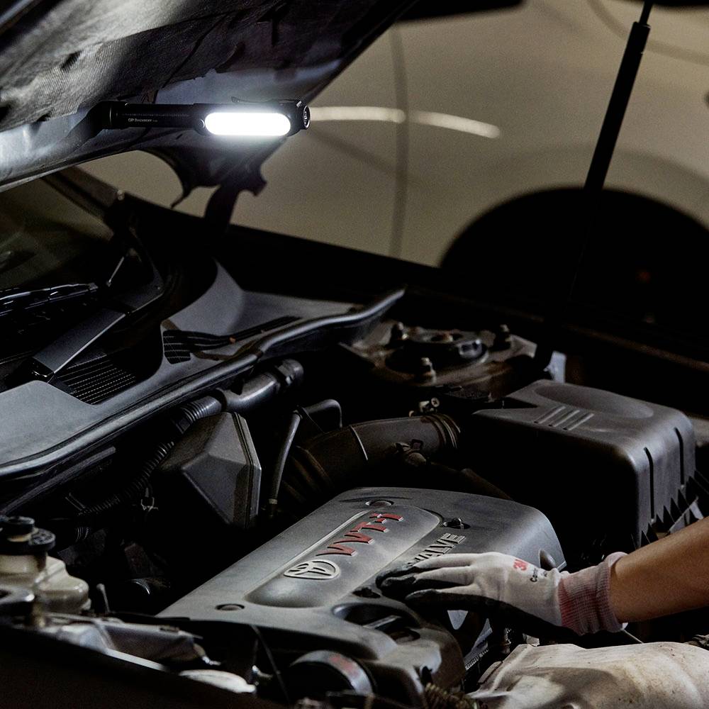 Ein Mechaniker arbeitet am Motor eines Autos in einer Werkstatt, die Motorhaube ist geöffnet.