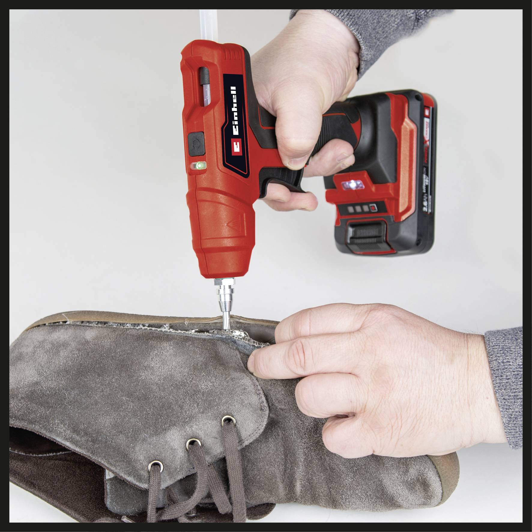 Eine Person näht eine graue Stiefelkante mit einem roten, kabellosen Handwerkzeug zusammen.