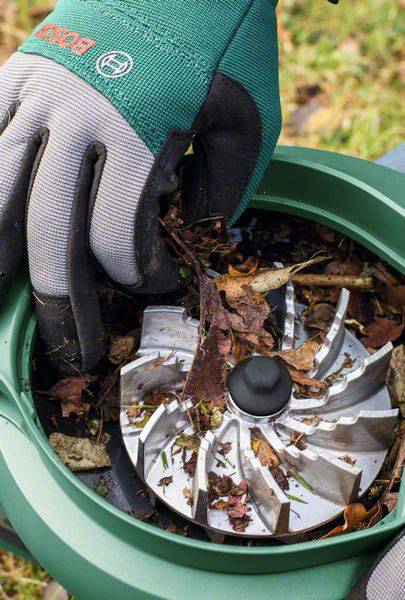 Eine behandschuhte Hand entfernt zerkleinertes Laub aus einem Gartenhäcksler. Der Metallrotor ist sichtbar.