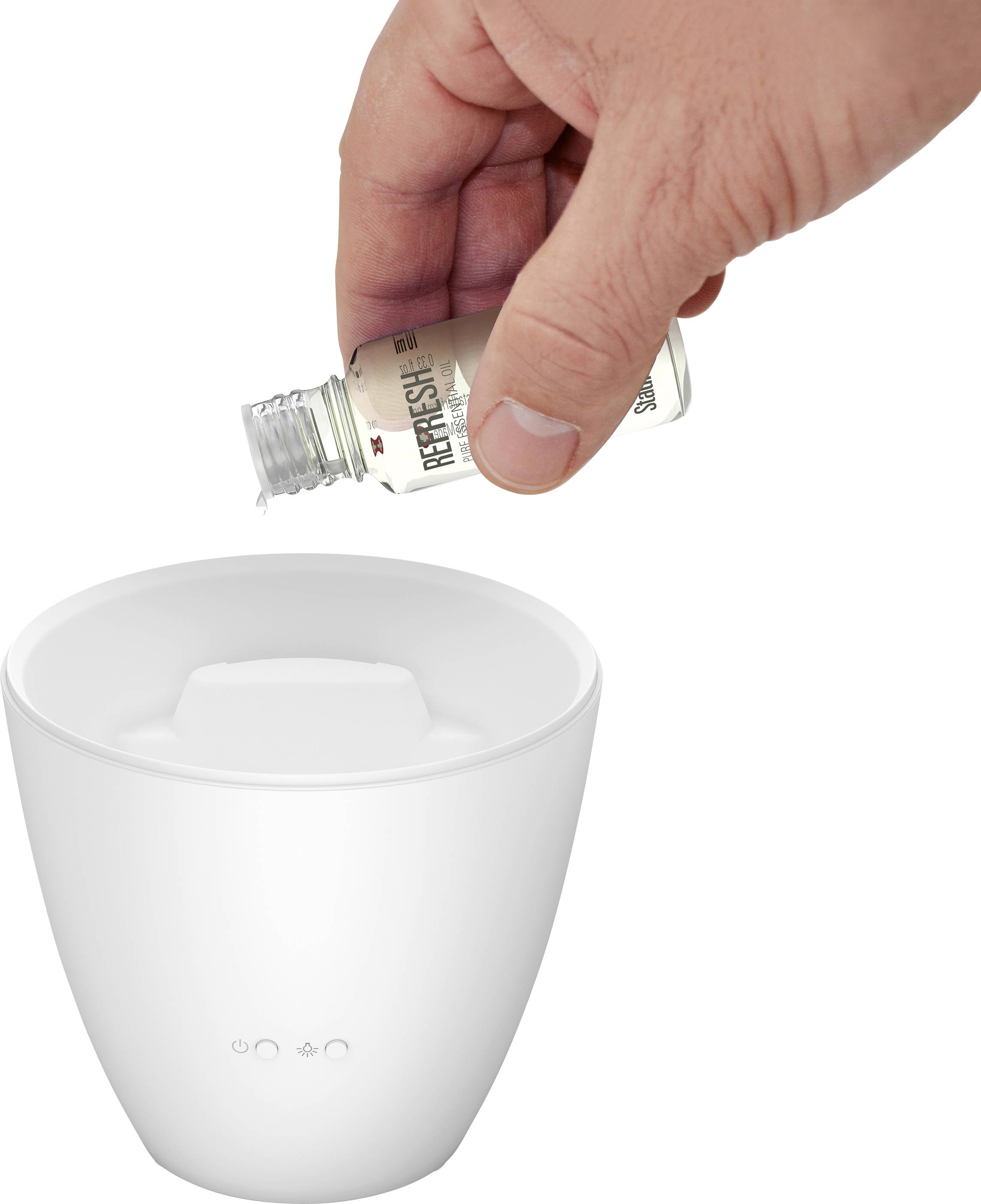 Hand gießt Duftöl in weißen Diffuser.