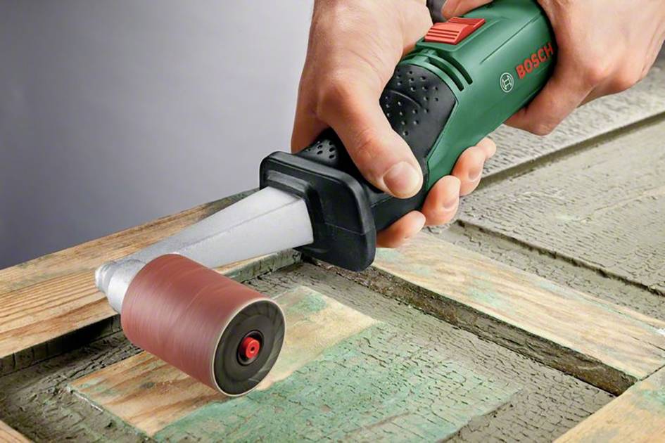 Eine Person schleift mit einem grünen Bosch-Elektrowerkzeug eine hölzerne Oberfläche ab.