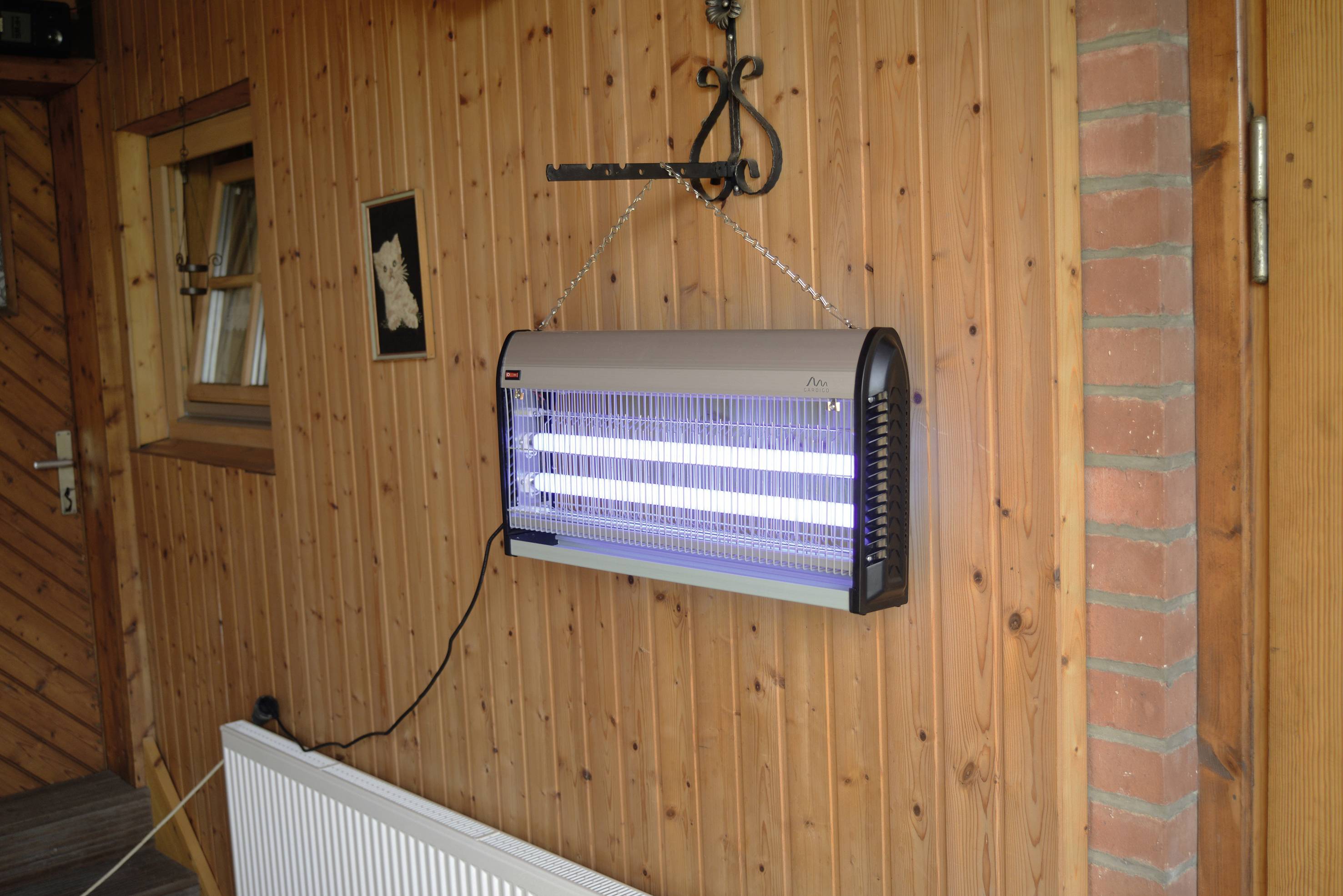 Elektrischer Insektenvernichter mit zwei Leuchtröhren hängt an einer Holzwand in einem Außenbereich.