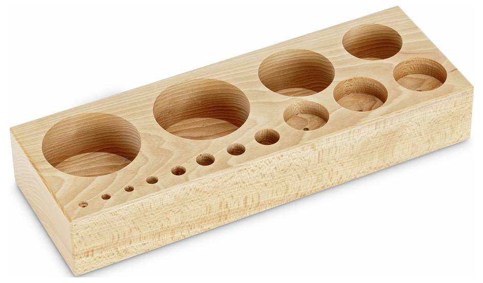Holzblock mit verschiedenen runden Vertiefungen in absteigender Größe, möglicherweise zur Aufbewahrung oder zum Sortieren von Gegenständen.