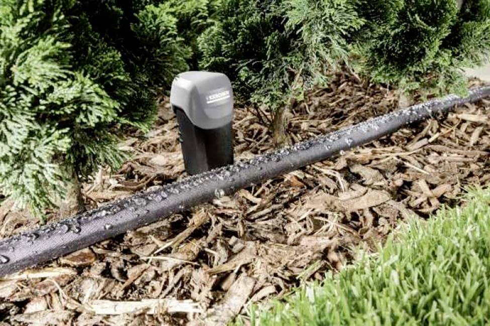 Bewässerungssystem in einem Garten: Ein Tropfrohr bewässert den Boden mit Pflanzen im Hintergrund, um Wasser effizient zu verteilen.