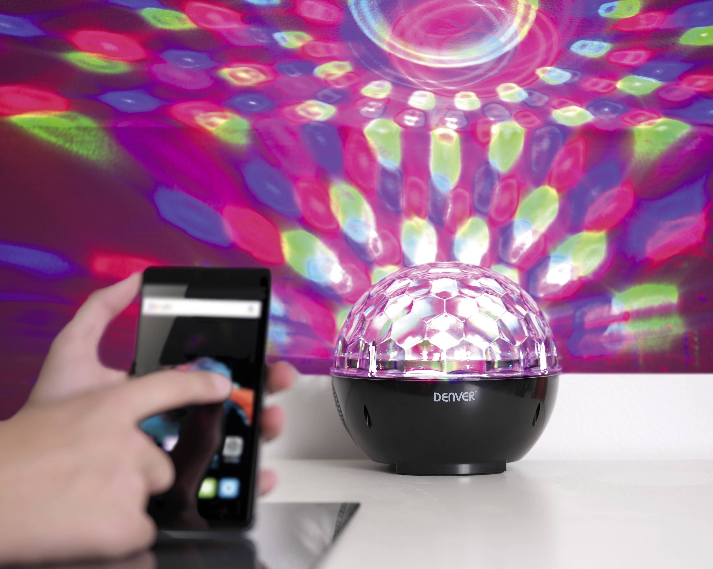 Eine bunte Lampe projiziert Muster an die Wand. Eine Person bedient ein Smartphone.